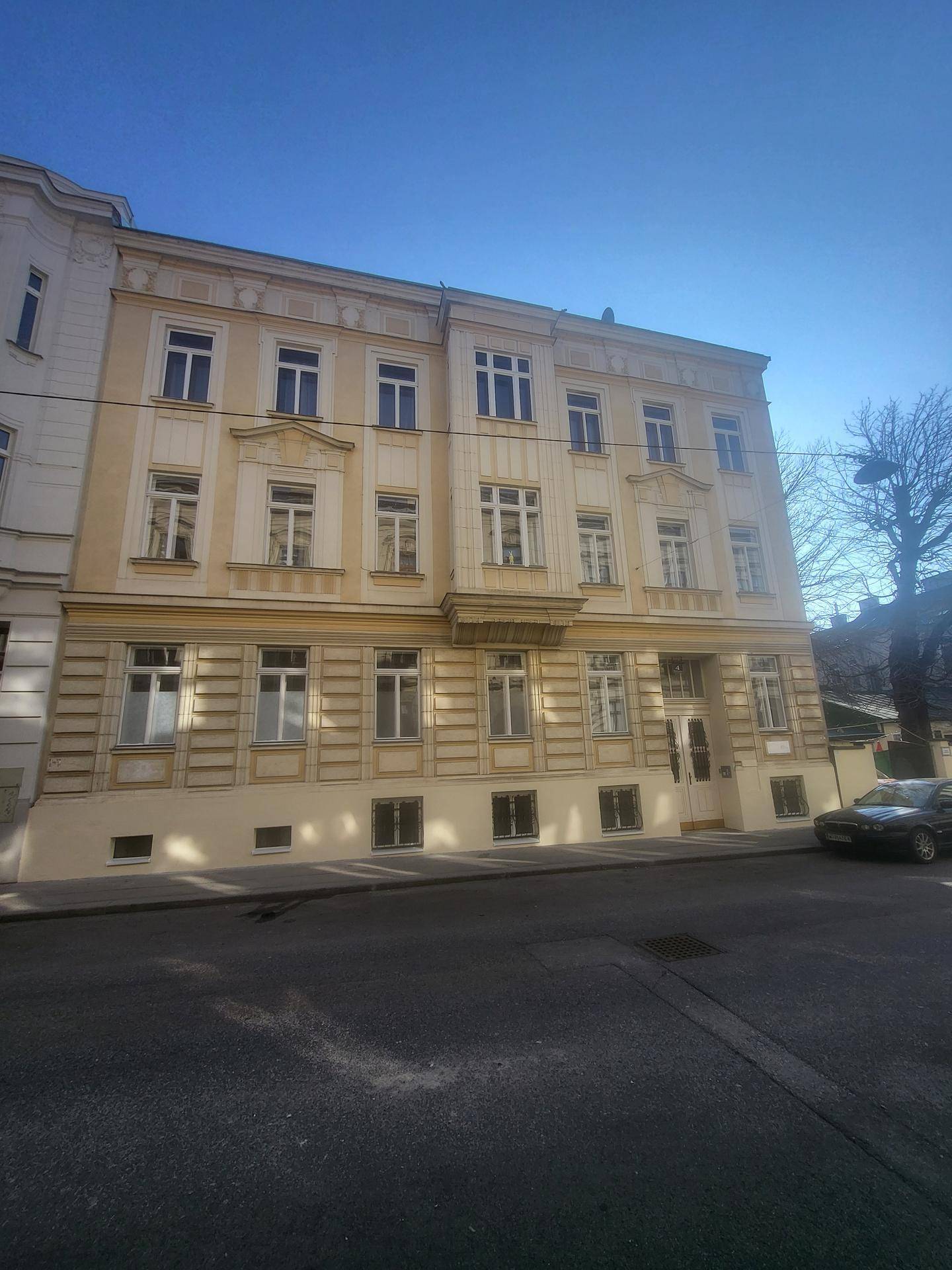 Klassische Fassade eines Mehrfamilienhauses mit vielen Fenstern und Balkon im Sonnenlicht.