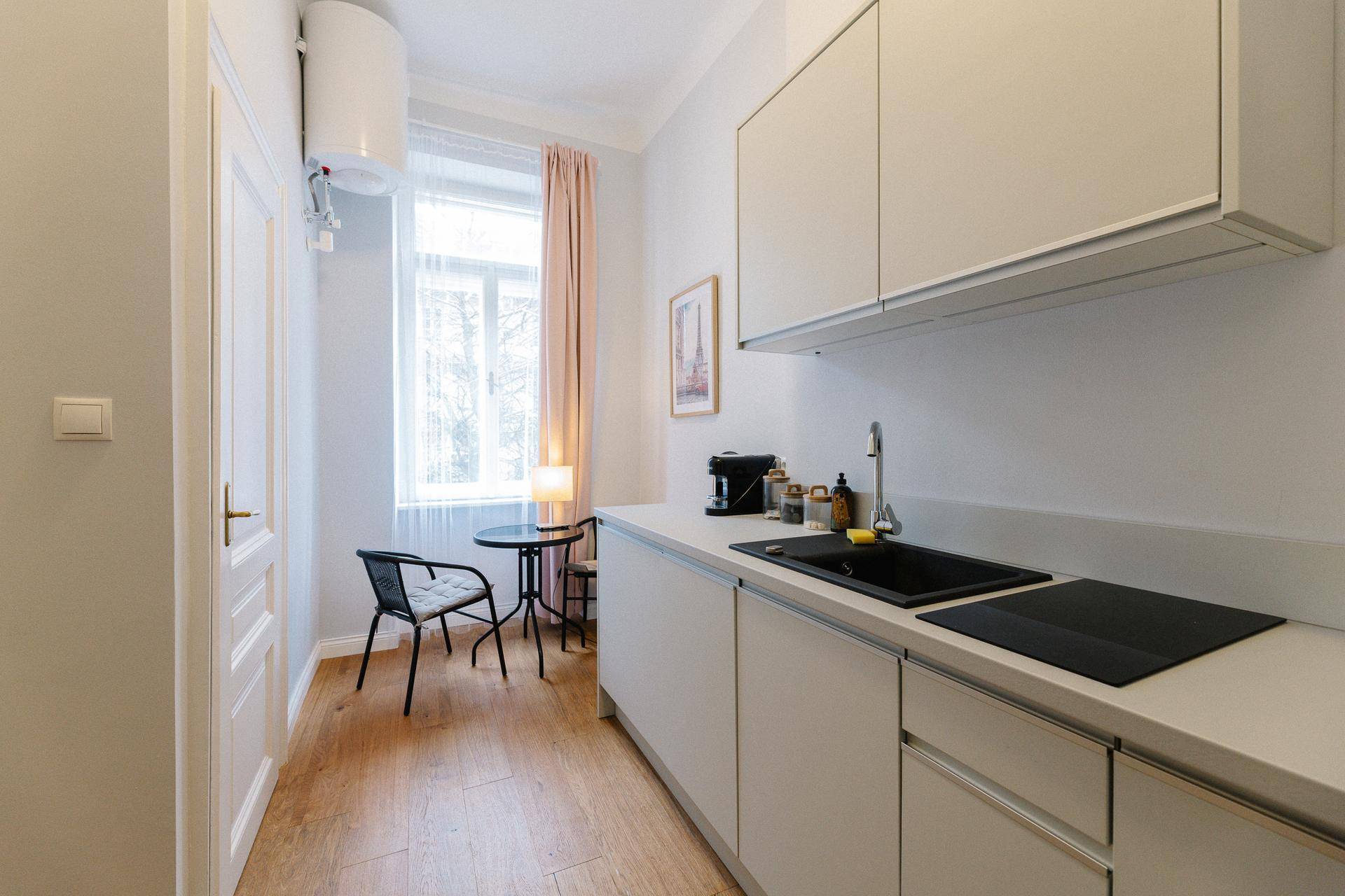 Moderne Küchenzeile mit hellen Schränken, Induktionskochfeld und kleinem Essbereich am Fenster.