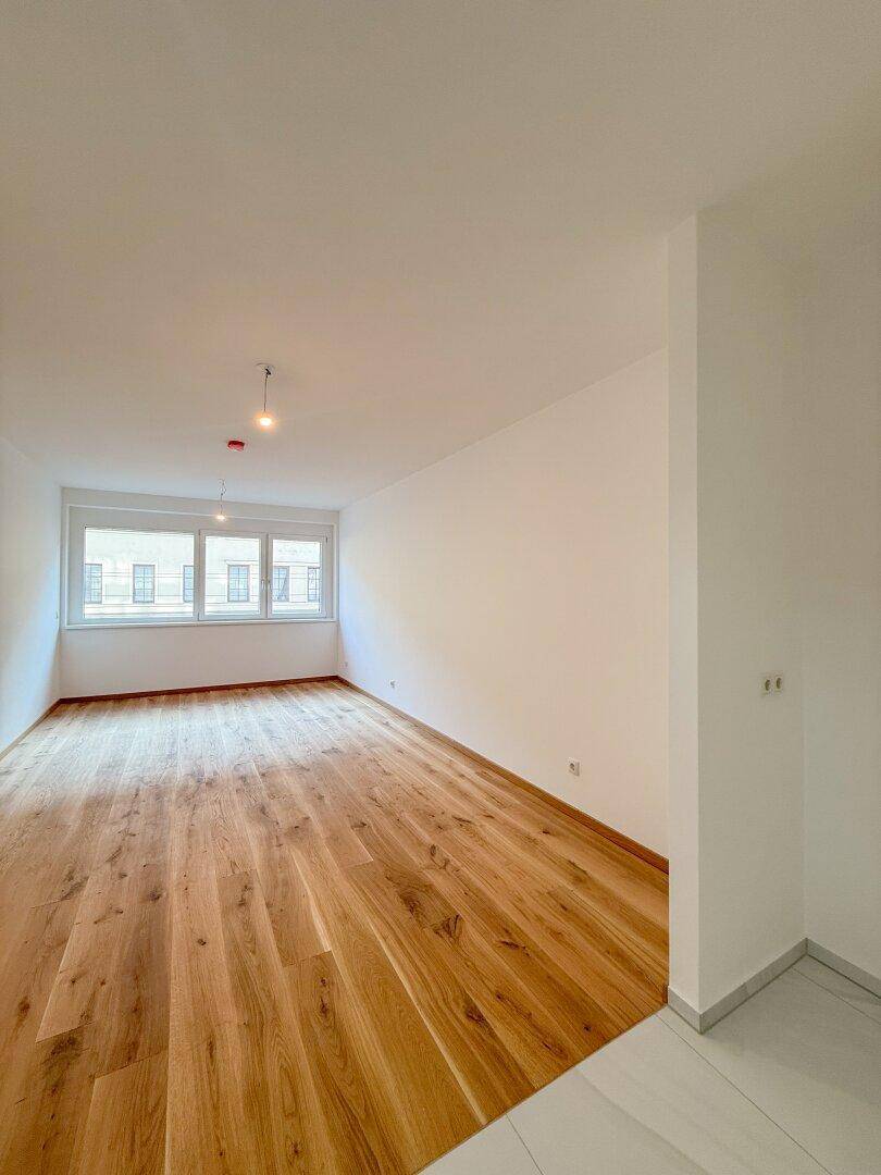 Helles, leeres Zimmer mit neuem Holzparkettboden und großen Fenstern, bereit zum Einzug.