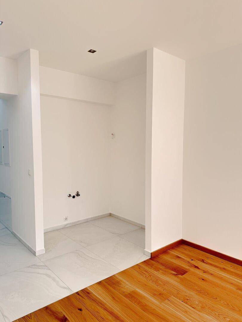 Vorbereiteter Küchenbereich mit Anschlüssen und Fliesenboden, bereit für die Installation einer Einbauküche.