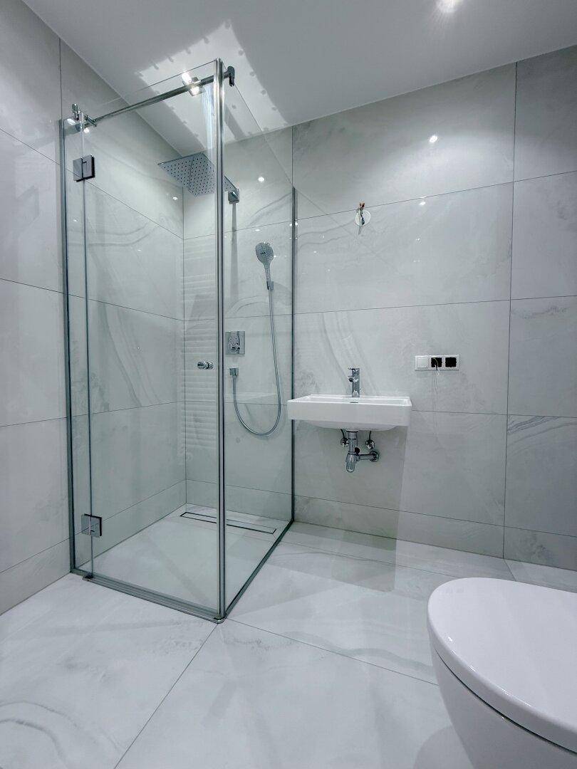 Modernes Badezimmer mit großformatigen Fliesen, einer Glasdusche und einer Regendusche für hohen Komfort.