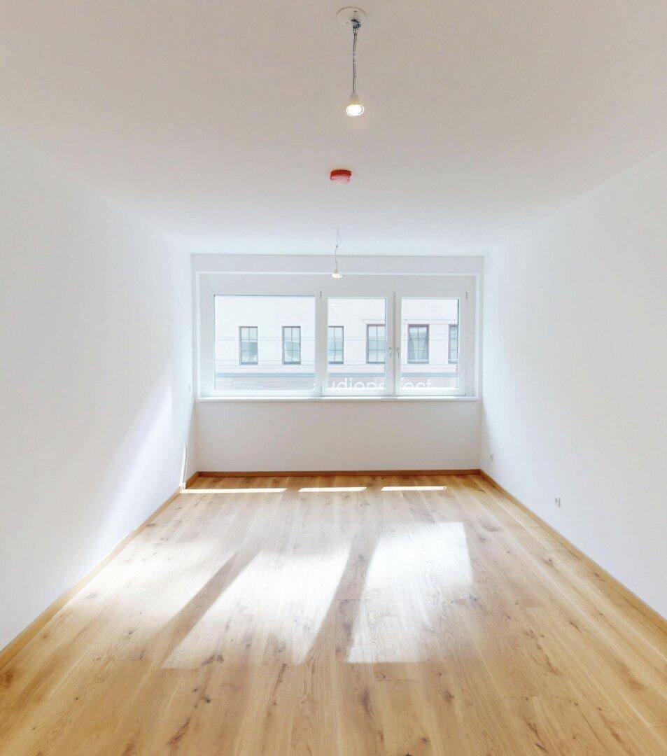 Heller, leerer Raum mit großen Fenstern und neuem Holzfußboden, ideal für Wohn- oder Schlafbereich.