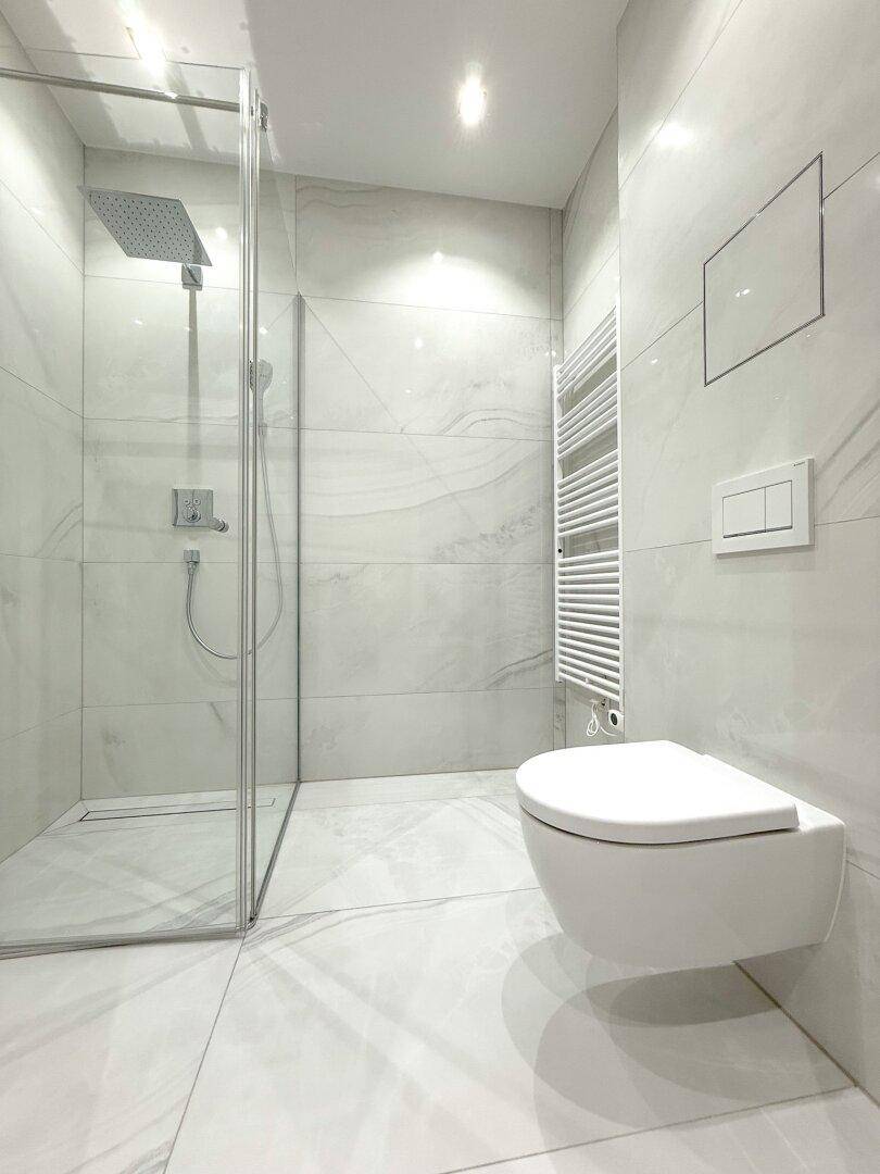 Modernes Badezimmer mit hellen Marmorfliesen, einer begehbaren Dusche und wandhängendem WC.