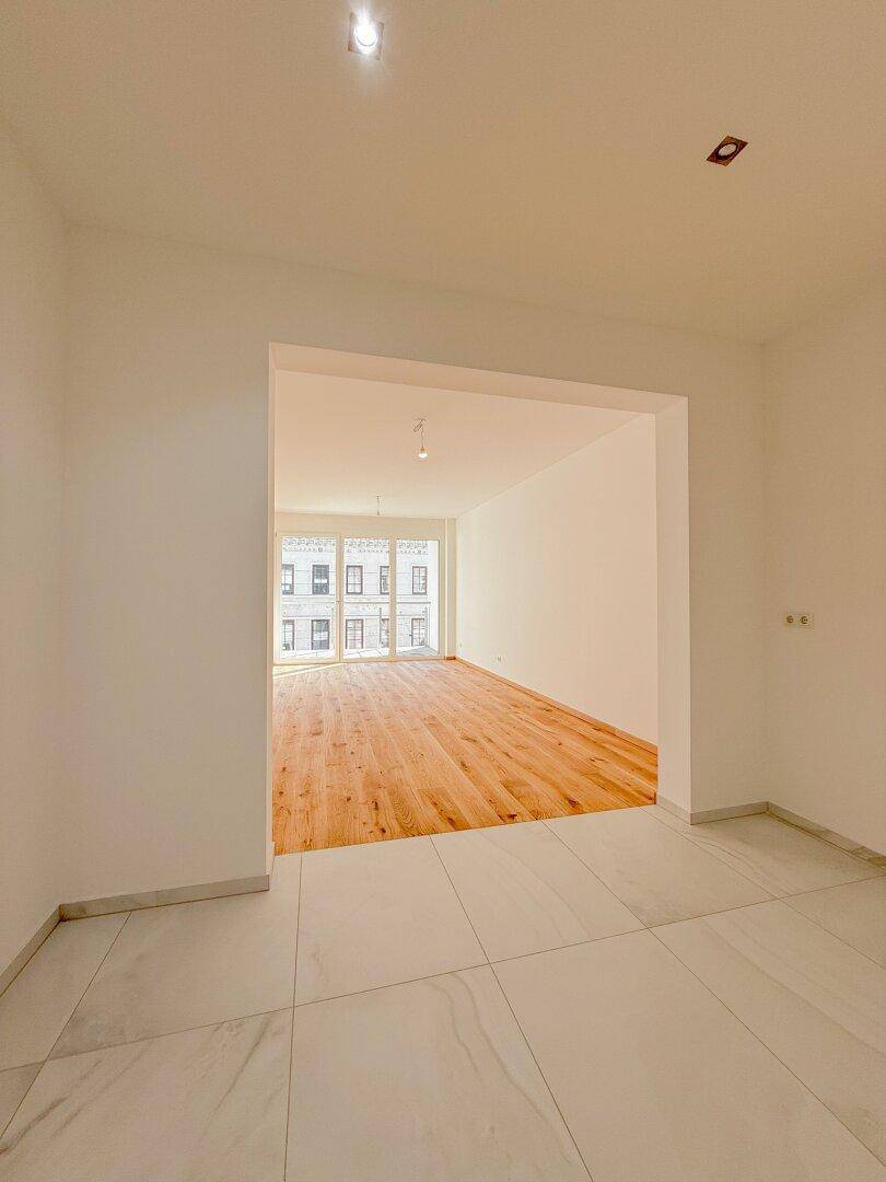 Heller Eingangsbereich mit modernen Fliesen, der in einen Raum mit Holzfußboden und großen Fenstern führt.