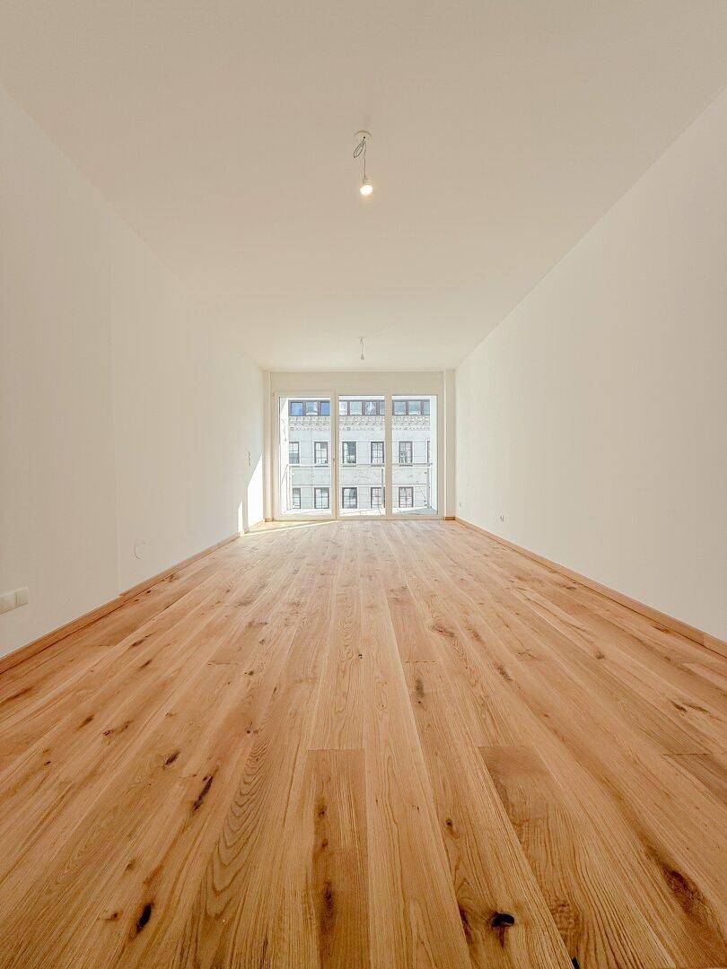 Lichtdurchfluteter, leerer Raum mit hellem Holzfußboden und großen Fenstern mit Stadtblick.