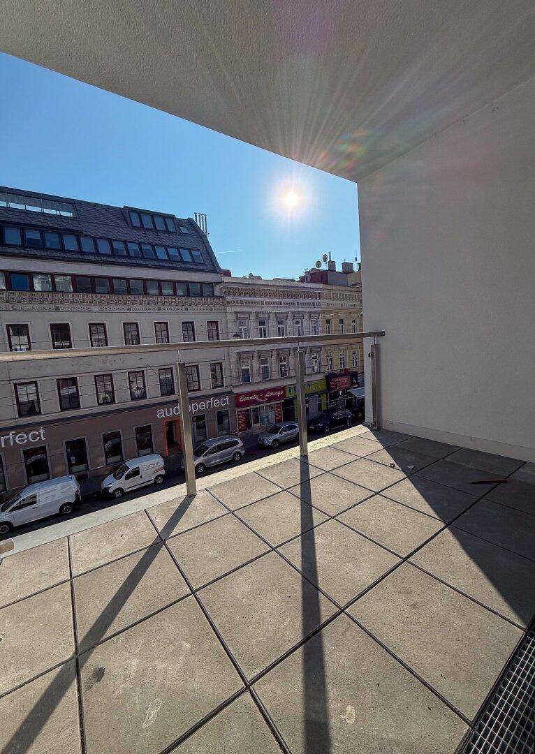 Heller Balkon mit Fliesenboden und Glasgeländer, bietet einen sonnigen Blick auf die Stadt.