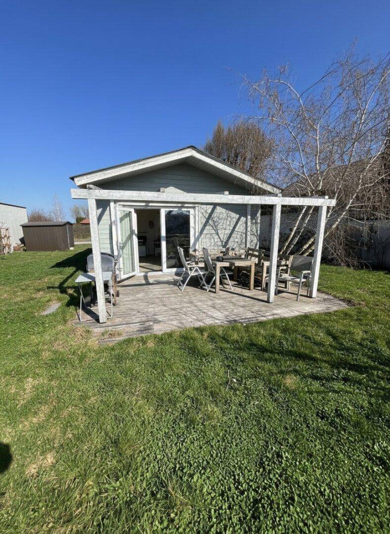 Kleines Gartenhaus mit überdachter Holzterrasse und Esstisch im Grünen.