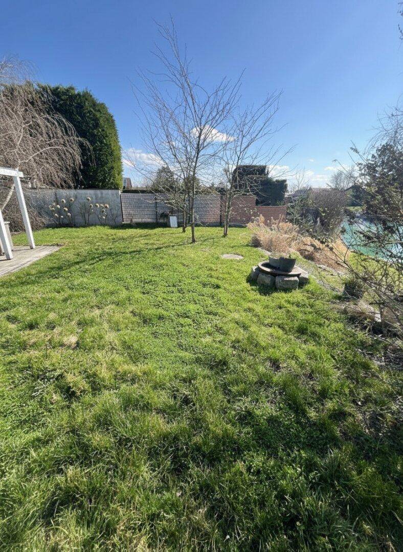 Weitläufiger Garten mit Rasenfläche, Bäumen und einer Feuerstelle.