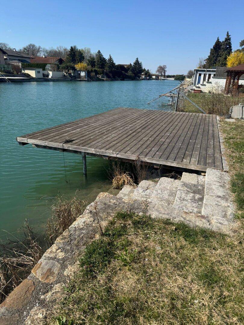Holzsteg am Wasser mit Steintreppe vom Ufer, ideal für den Zugang zum Kanal.
