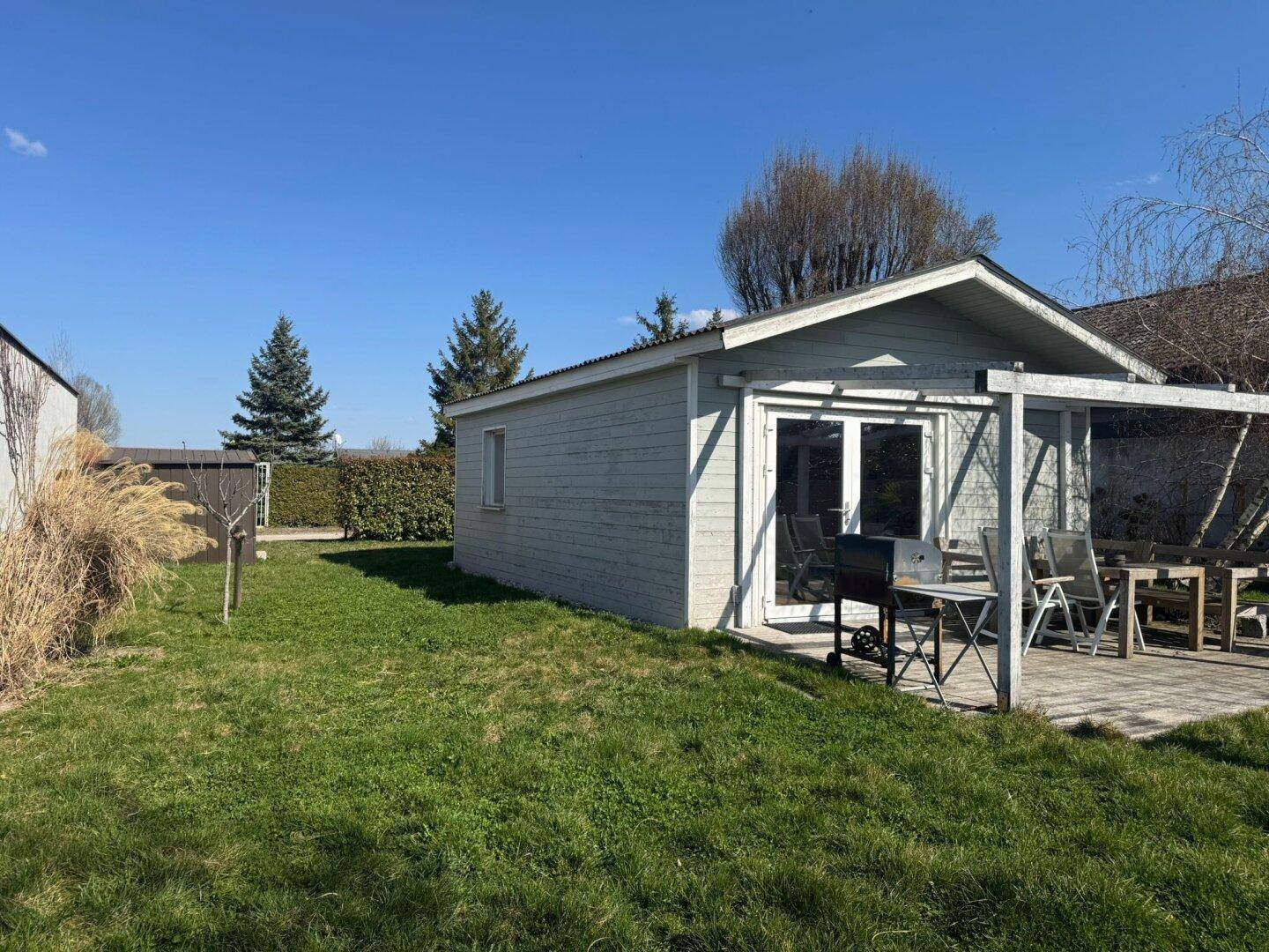 Seitenansicht des Gartenhauses mit Terrasse, Grill und weitläufiger Rasenfläche.