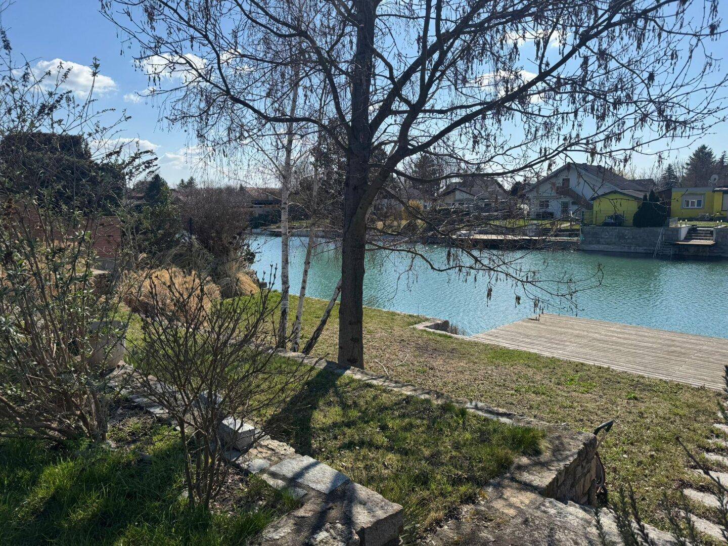 Gartenbereich mit Bäumen und Blick auf den Kanal sowie die Häuser auf der gegenüberliegenden Seite.