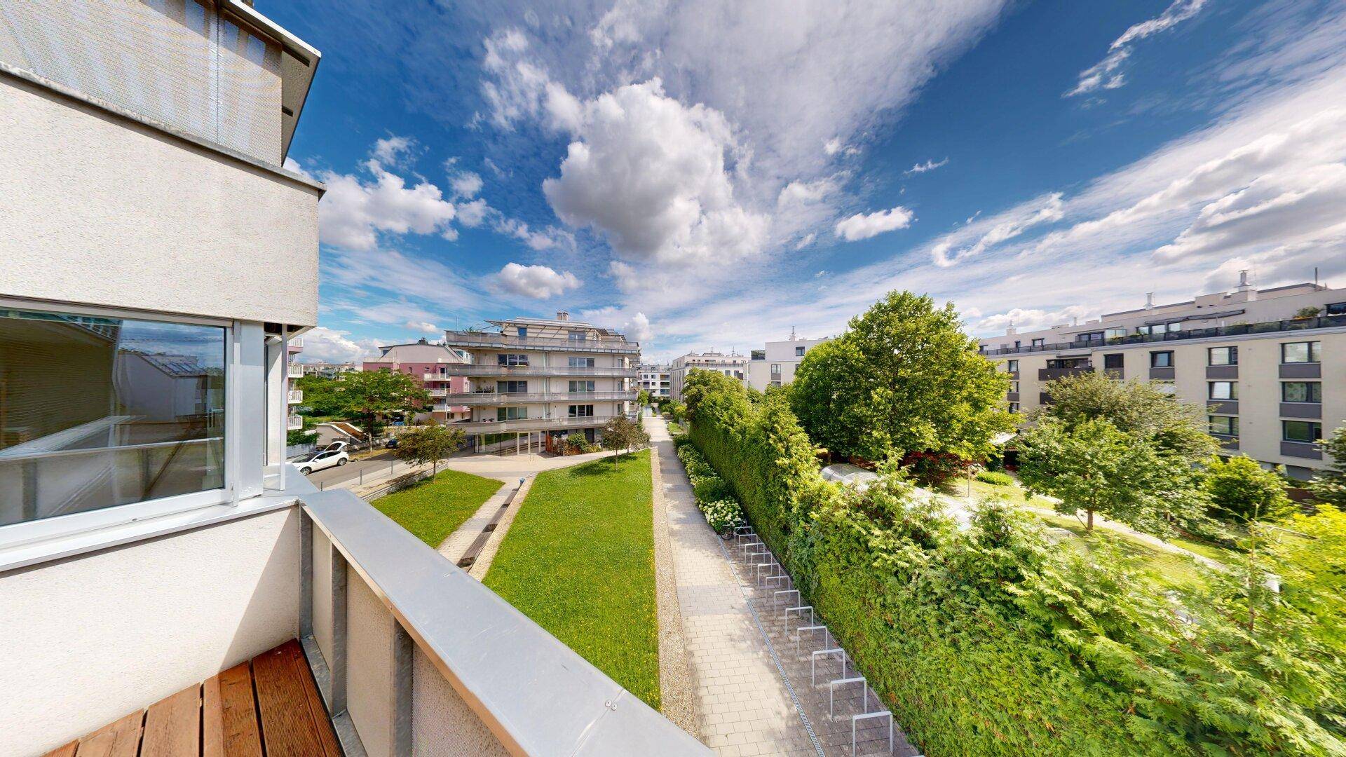 Weitläufiger Blick vom Balkon auf eine grüne Parkanlage und umliegende Wohngebäude.