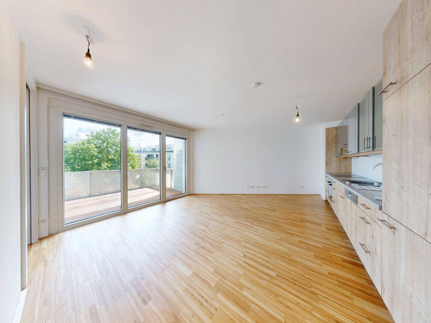 Offener Wohnbereich mit Holzboden und Zugang zum Balkon, angrenzend an eine moderne Küche.