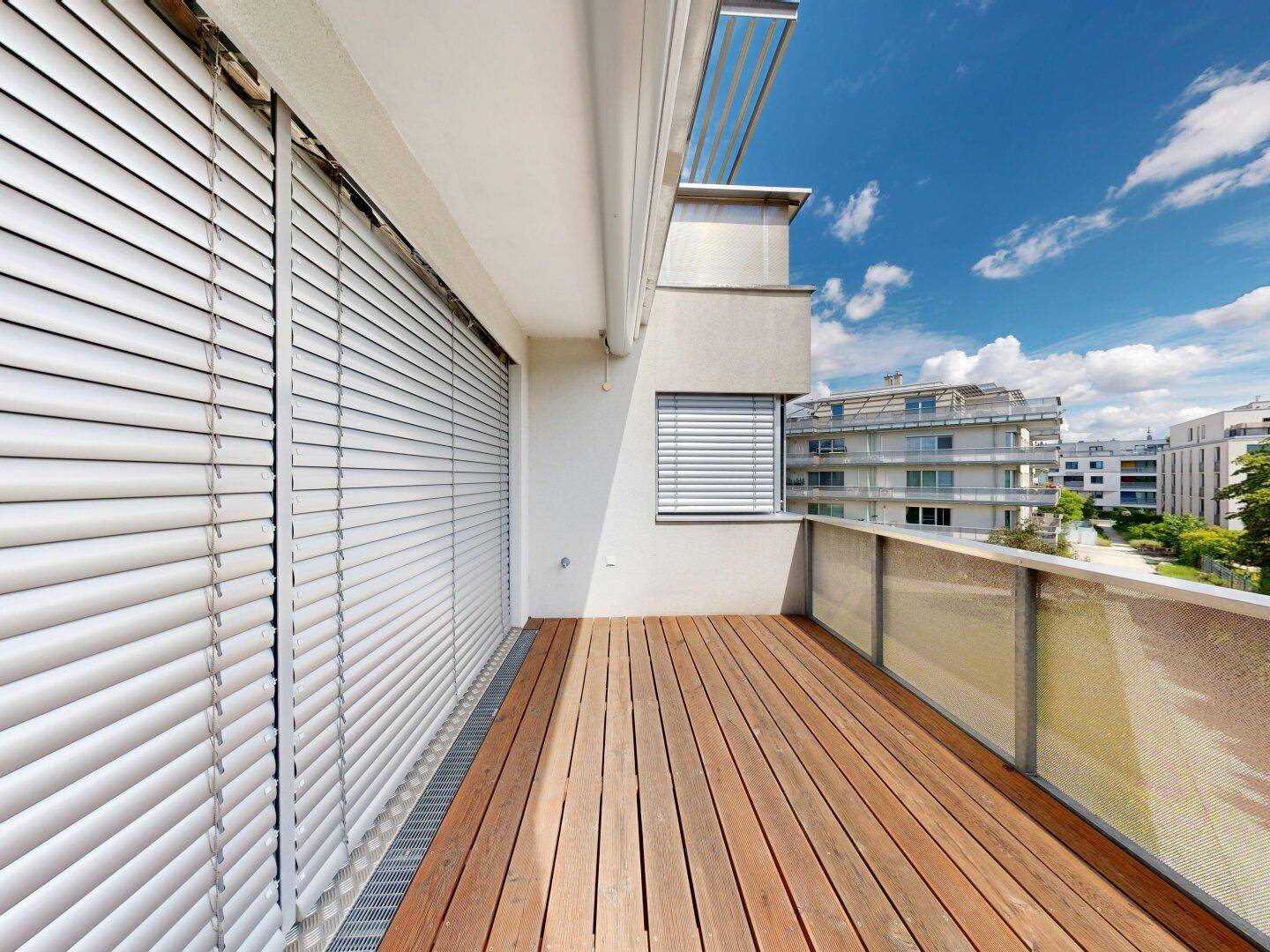Heller Balkon mit Holzboden und geschlossenen Rollläden, bietet Privatsphäre und Schutz.