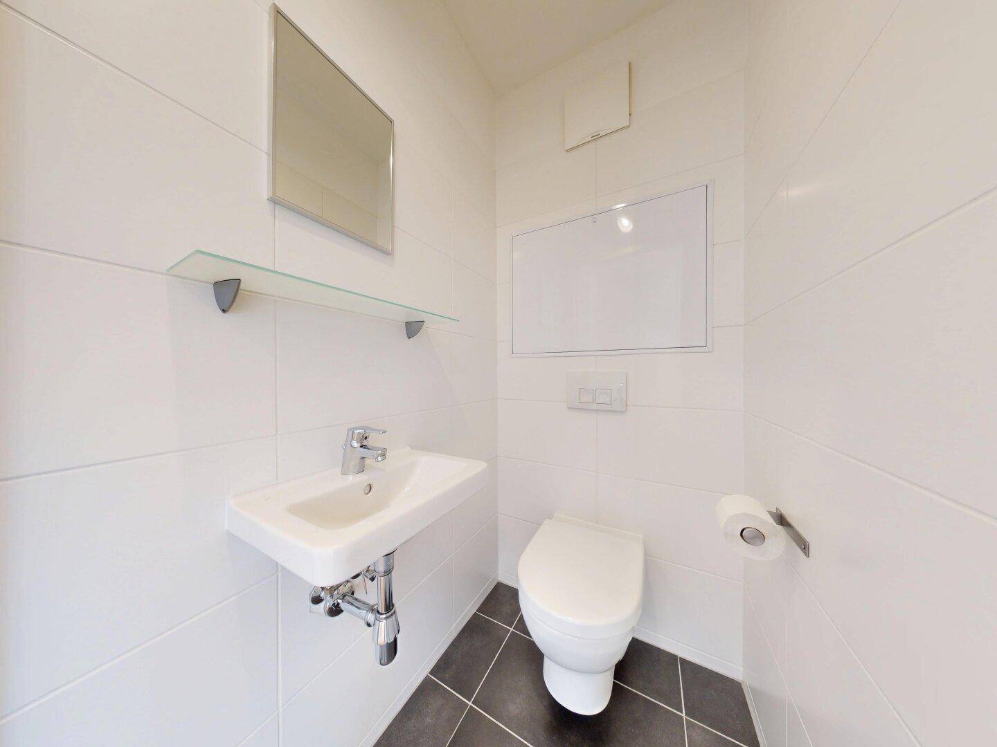 Helles Gäste-WC mit modernen Fliesen, wandhängendem WC und kleinem Waschbecken.