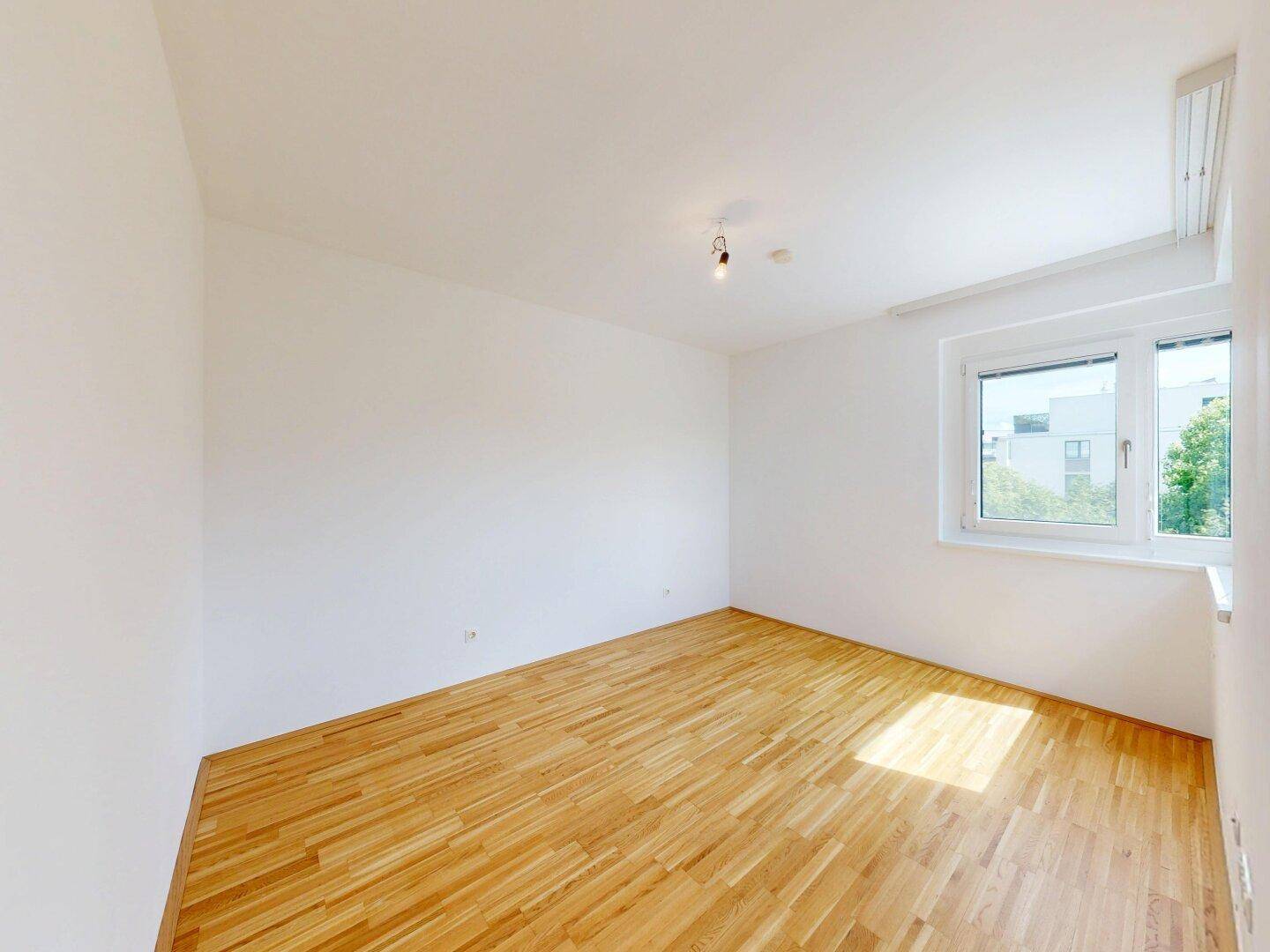 Heller, leerer Raum mit Holzboden und Fenster, vielseitig nutzbar als Schlaf- oder Arbeitszimmer.