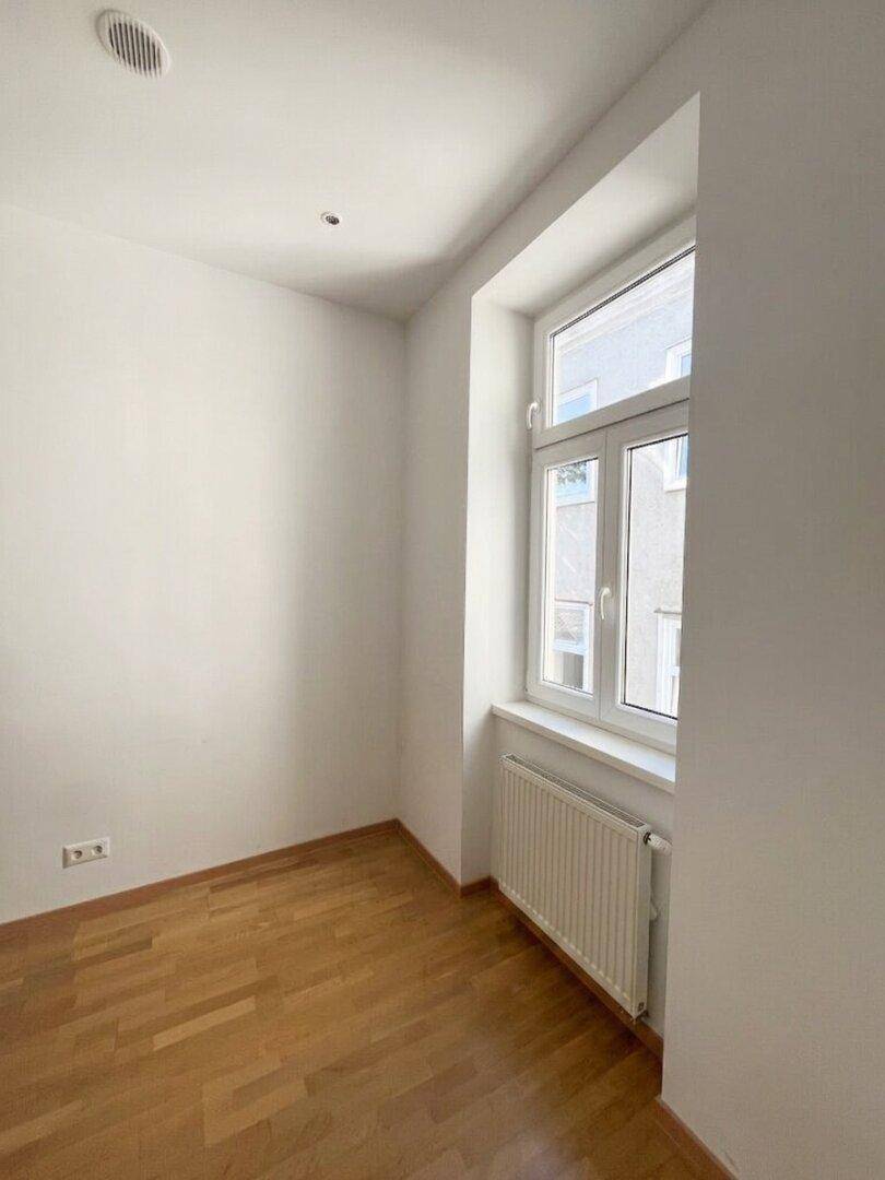 Heller Raum mit Parkettboden und großem Fenster, ideal für Schlaf- oder Arbeitszimmer.