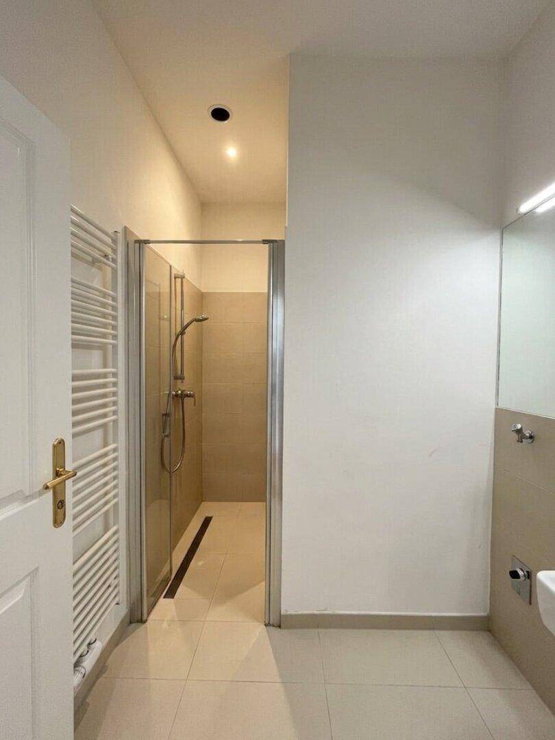 Helles Badezimmer mit begehbarer Dusche, Handtuchheizkörper und Fliesenboden.