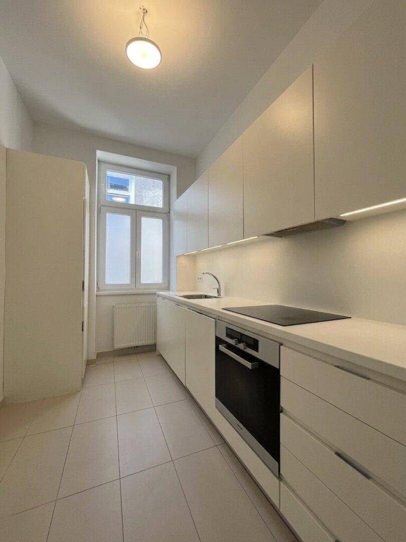 Moderne Einbauküche mit weißen Schränken, Induktionskochfeld und integriertem Backofen.