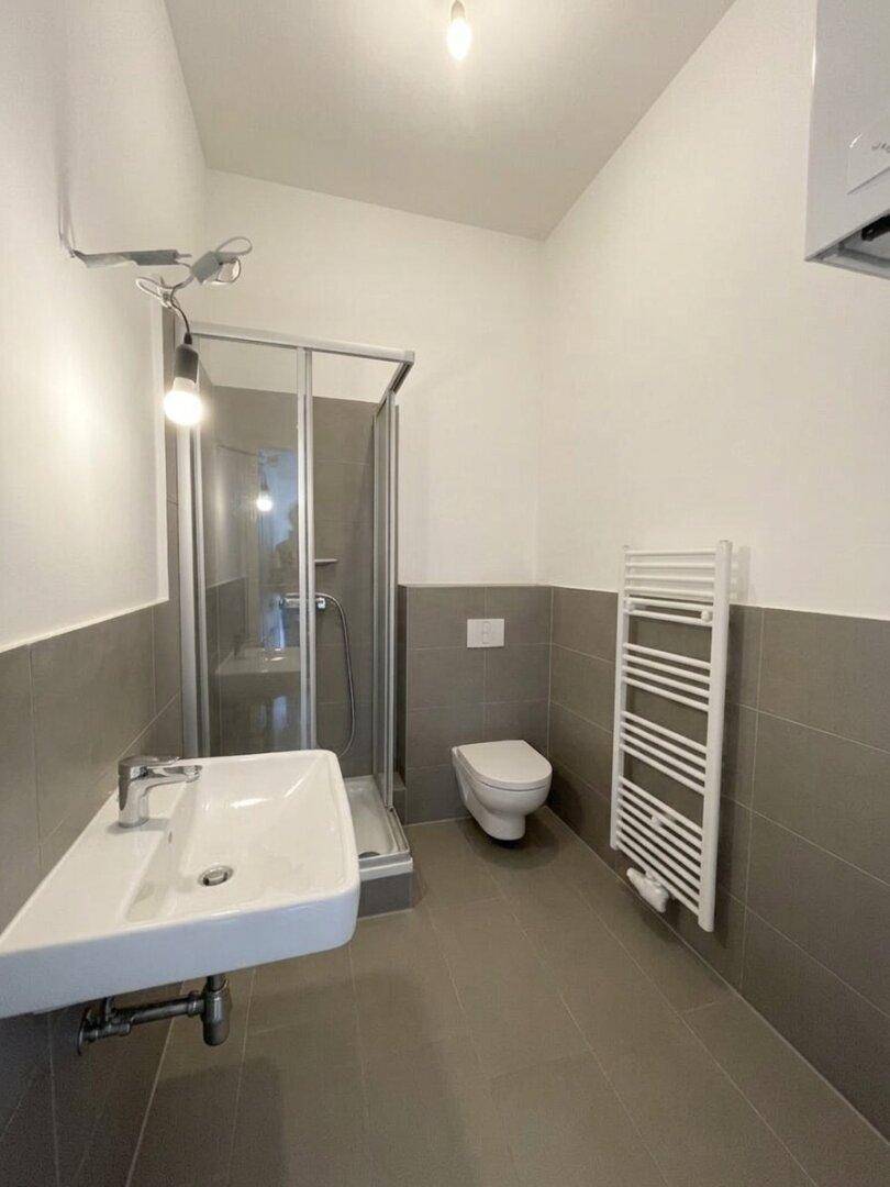 Modernes Badezimmer mit Duschkabine, wandhängendem WC, Waschbecken und Handtuchheizkörper.