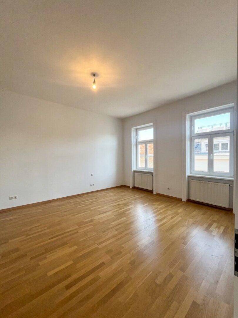 Geräumiger, heller Raum mit Parkettboden und zwei Fenstern, vielseitig nutzbar.