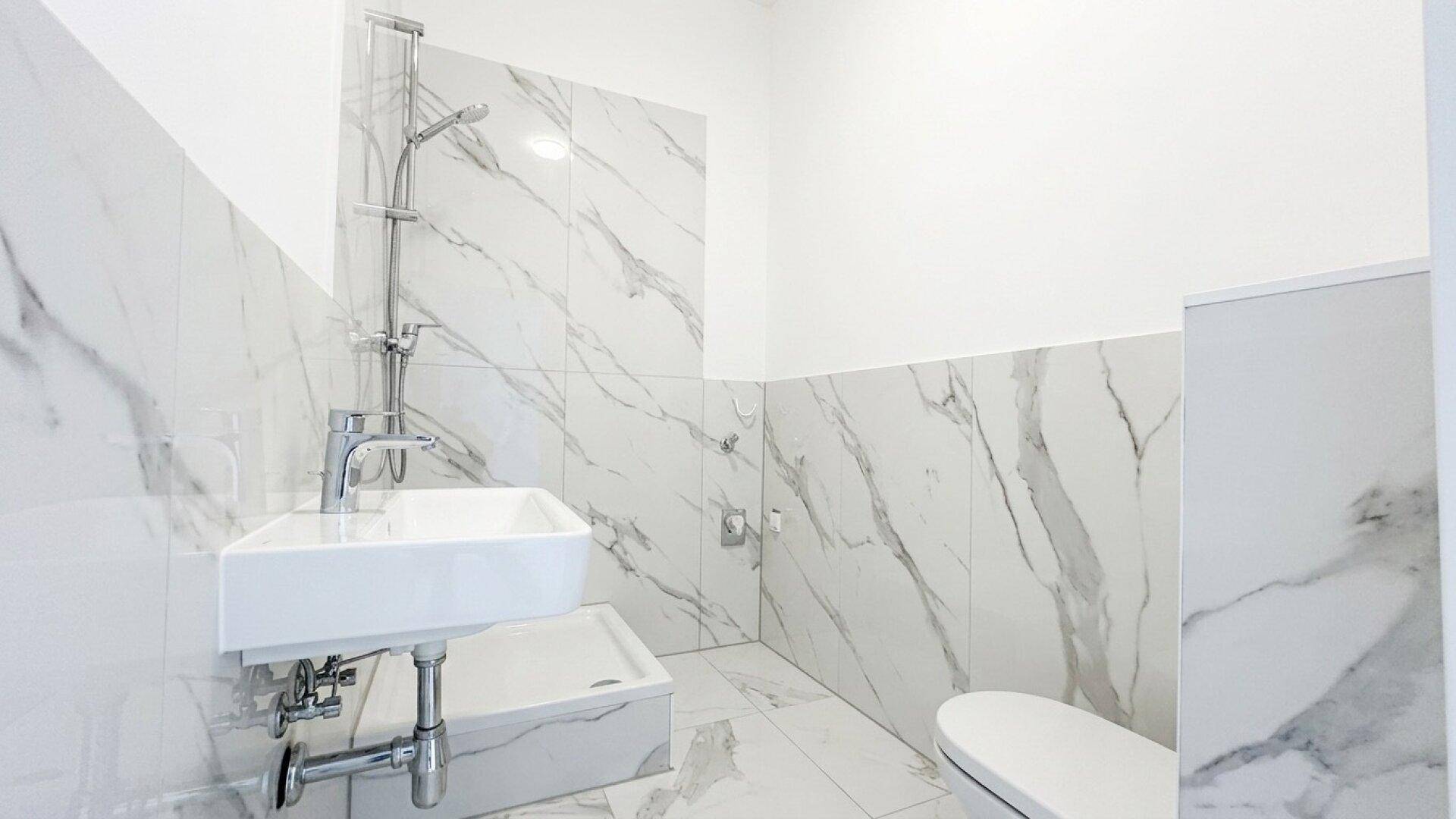 Kleines Badezimmer mit Marmorfliesen, wandmontiertem Waschbecken und Toilette.