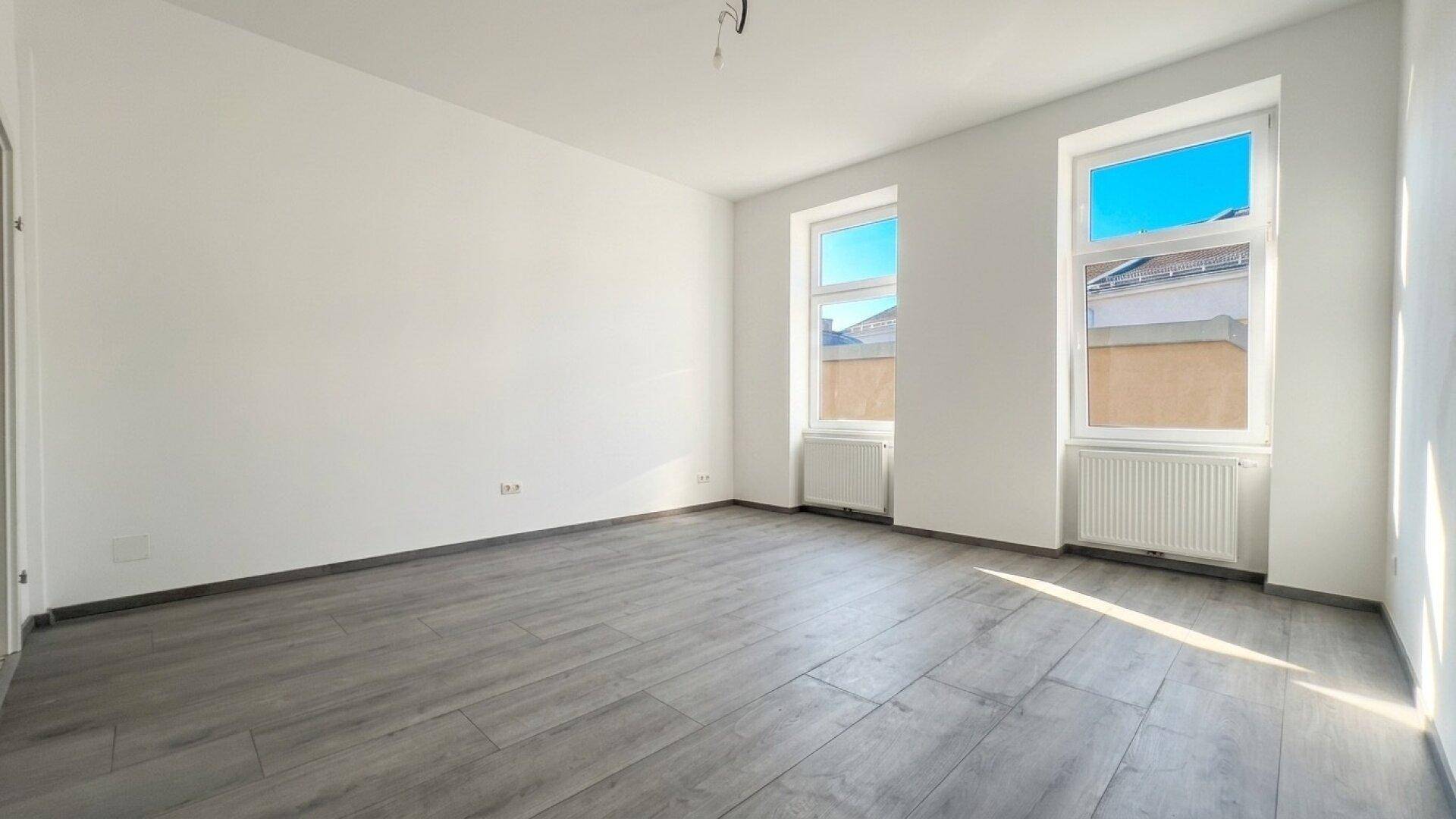 Geräumiger, heller Raum mit großen Fenstern und modernem Laminatboden.