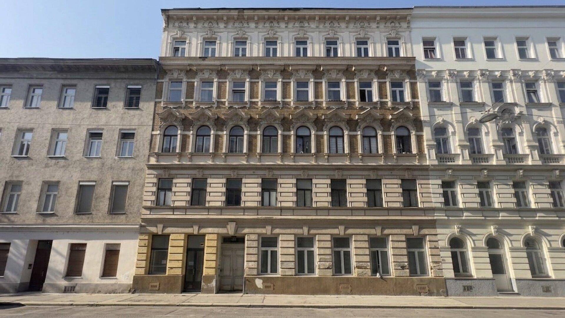 Historische Fassade eines Mehrfamilienhauses mit reich verzierten Details und vielen Fenstern in einer Stadtansicht.
