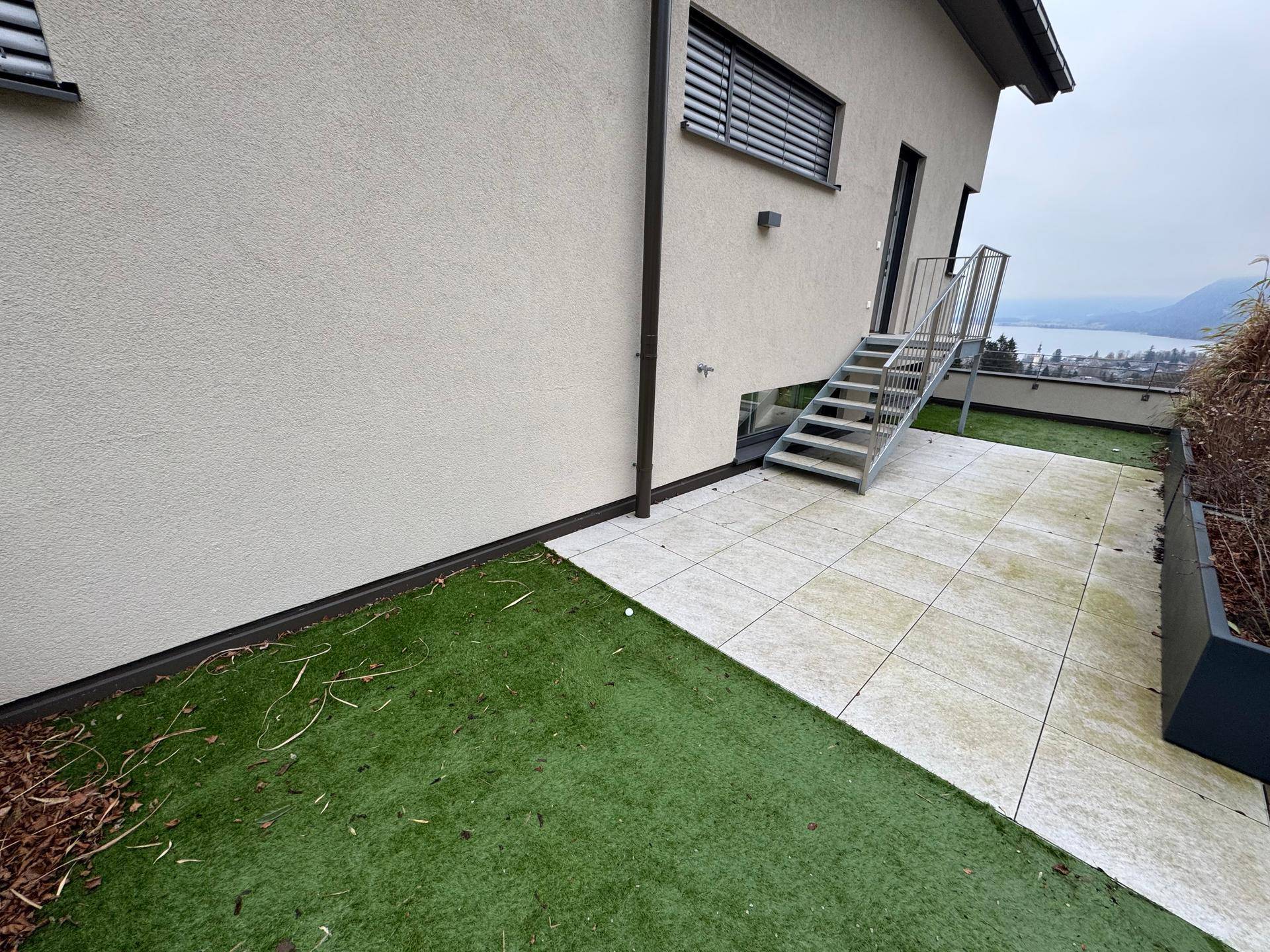 Große Terrasse mit Kunstrasen und Treppe, die zu einem weiteren Außenbereich führt.