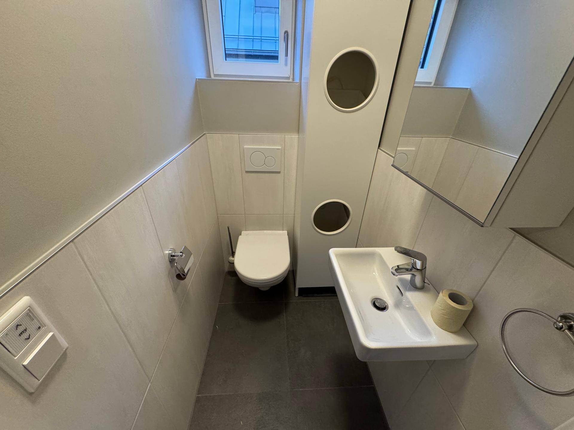Kleines Gäste-WC mit modernem Waschbecken, wandhängender Toilette und Fenster.