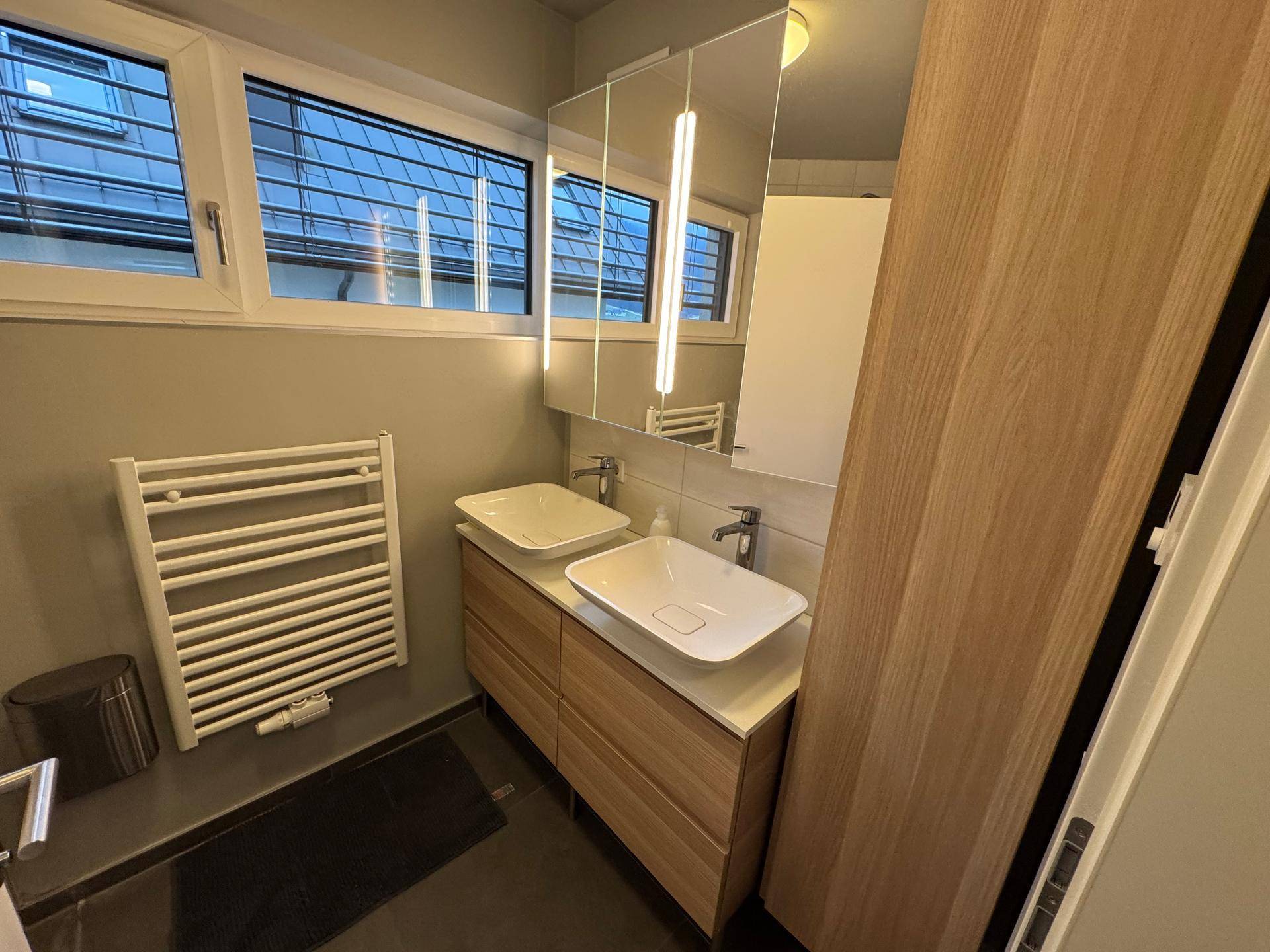 Modernes Badezimmer mit Doppelwaschbecken, Spiegelschrank und beheiztem Handtuchhalter.