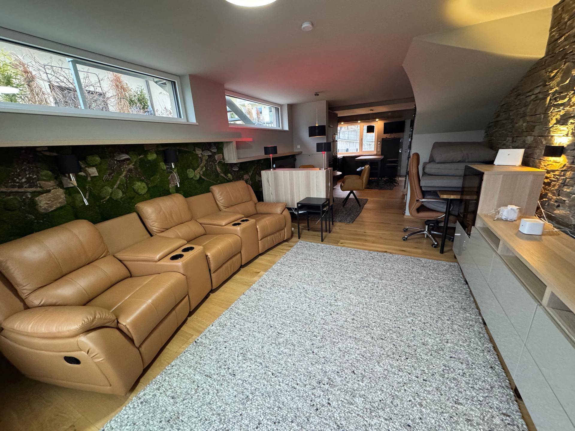 Geräumiger Wohnbereich mit bequemen Ledersofas, Holzboden und einer dekorativen Steinwand.