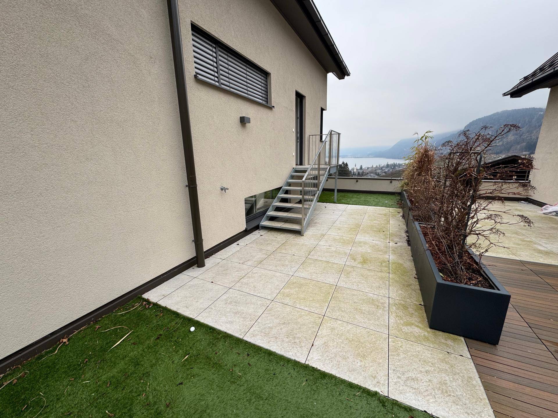 Geräumige Terrasse mit Fliesen und Holzboden, umgeben von Pflanzenkübeln und Seeblick.