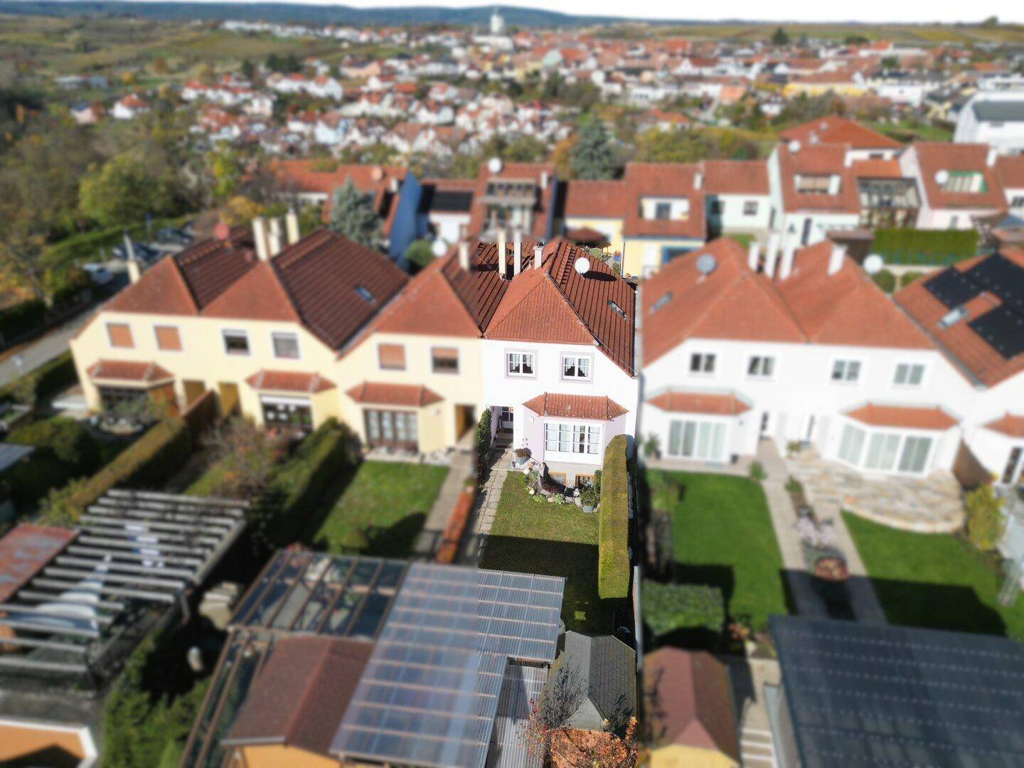 Luftaufnahme einer Wohnsiedlung mit Reihenhäusern, Gärten und Blick auf die umliegende Landschaft.
