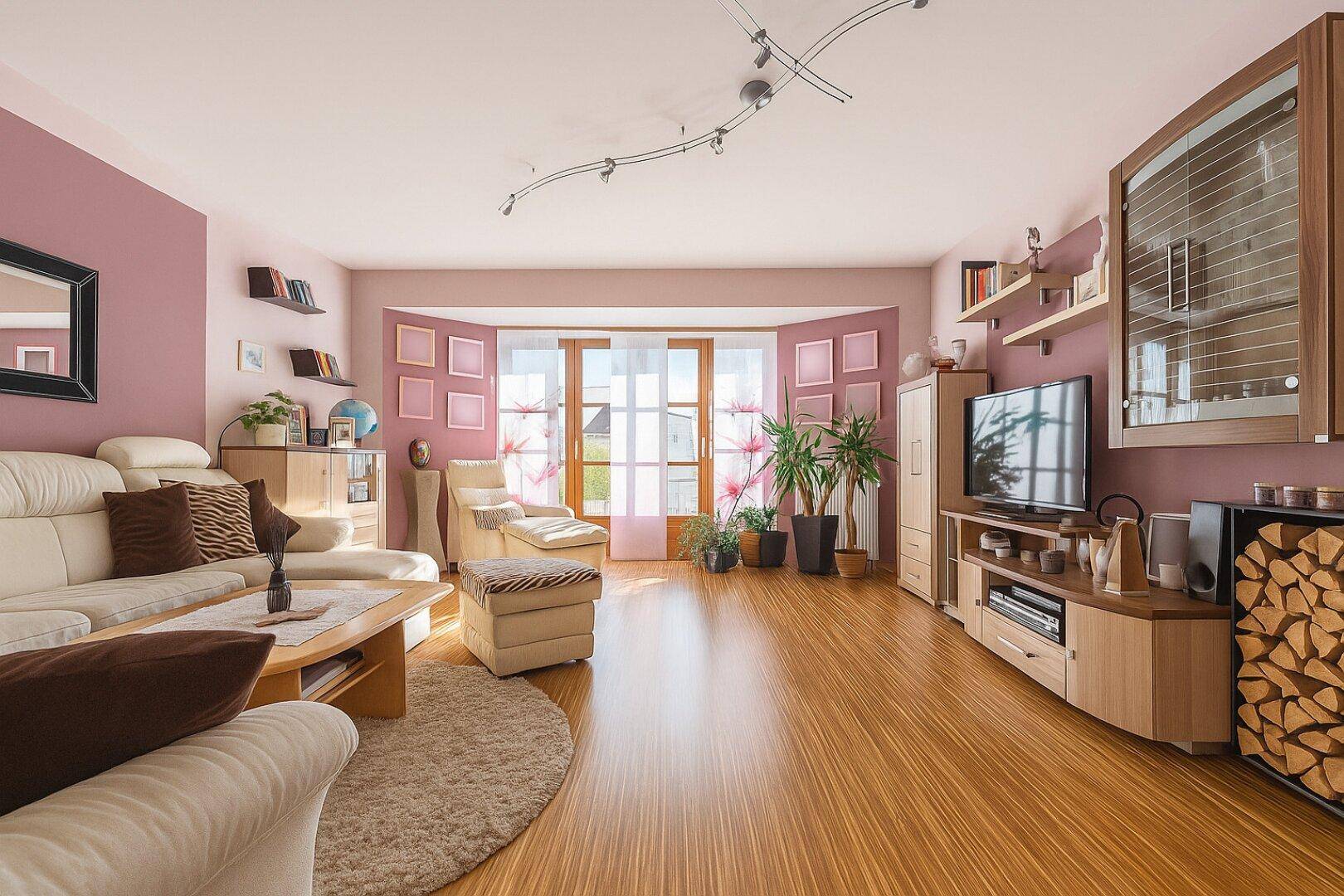 Gemütliches Wohnzimmer mit hellem Laminatboden, rosa Wänden und Zugang zu einem Erkerfensterbereich.