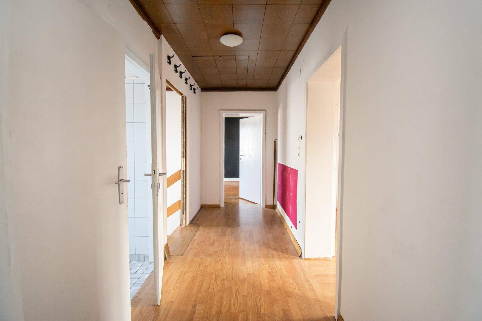 Heller Flur mit Holzdecke und Laminatboden, der zu verschiedenen Räumen führt.