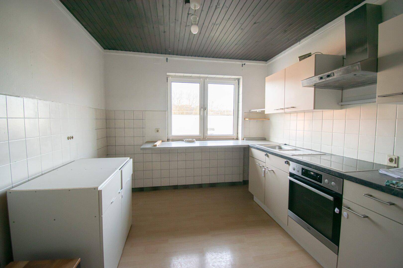 Unmöblierte Küche mit weißen Einbauschränken, dunkler Decke und einem Fenster.
