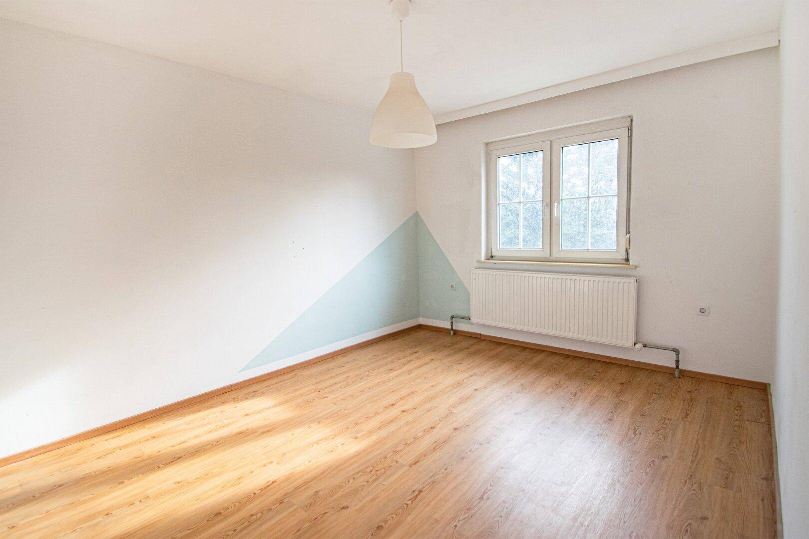 Leeres Schlafzimmer mit Laminatboden, weißen Wänden und einem Fenster für Tageslicht.