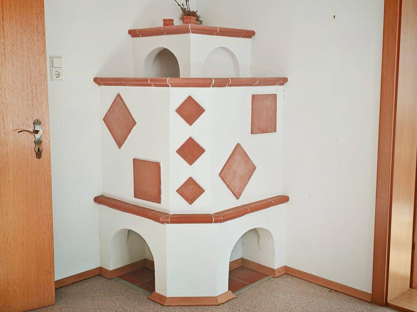 Traditioneller Kachelofen mit braunen Zierelementen in einer Ecke des Raumes.