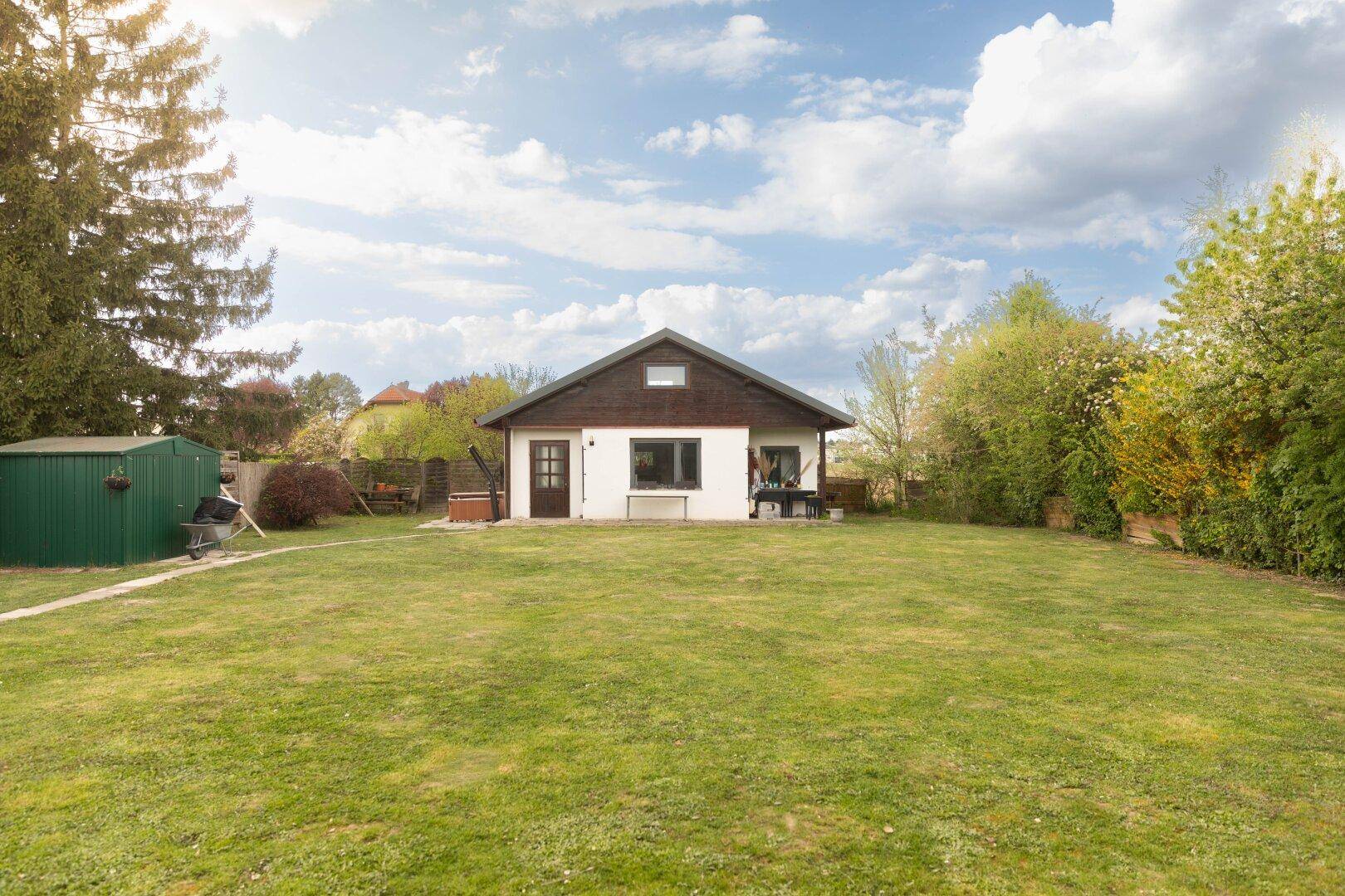 Großer grüner Garten mit Rasenfläche, einem kleinen Haus und Geräteschuppen im Hintergrund.