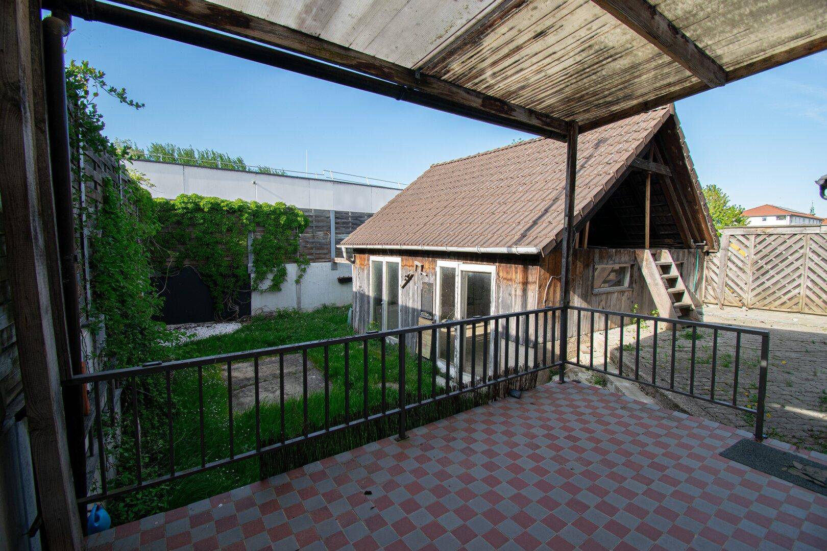 Überdachte Terrasse mit Fliesenboden und Blick auf den Gartenbereich mit Holzschuppen.