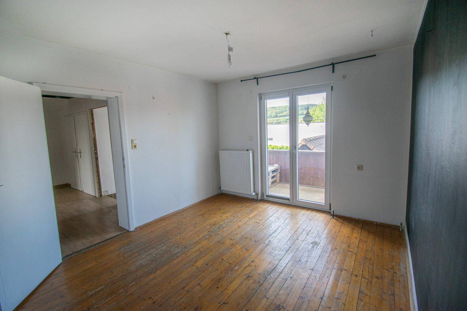 Helles Schlafzimmer mit Holzdielenboden und direktem Zugang zu einem Balkon.