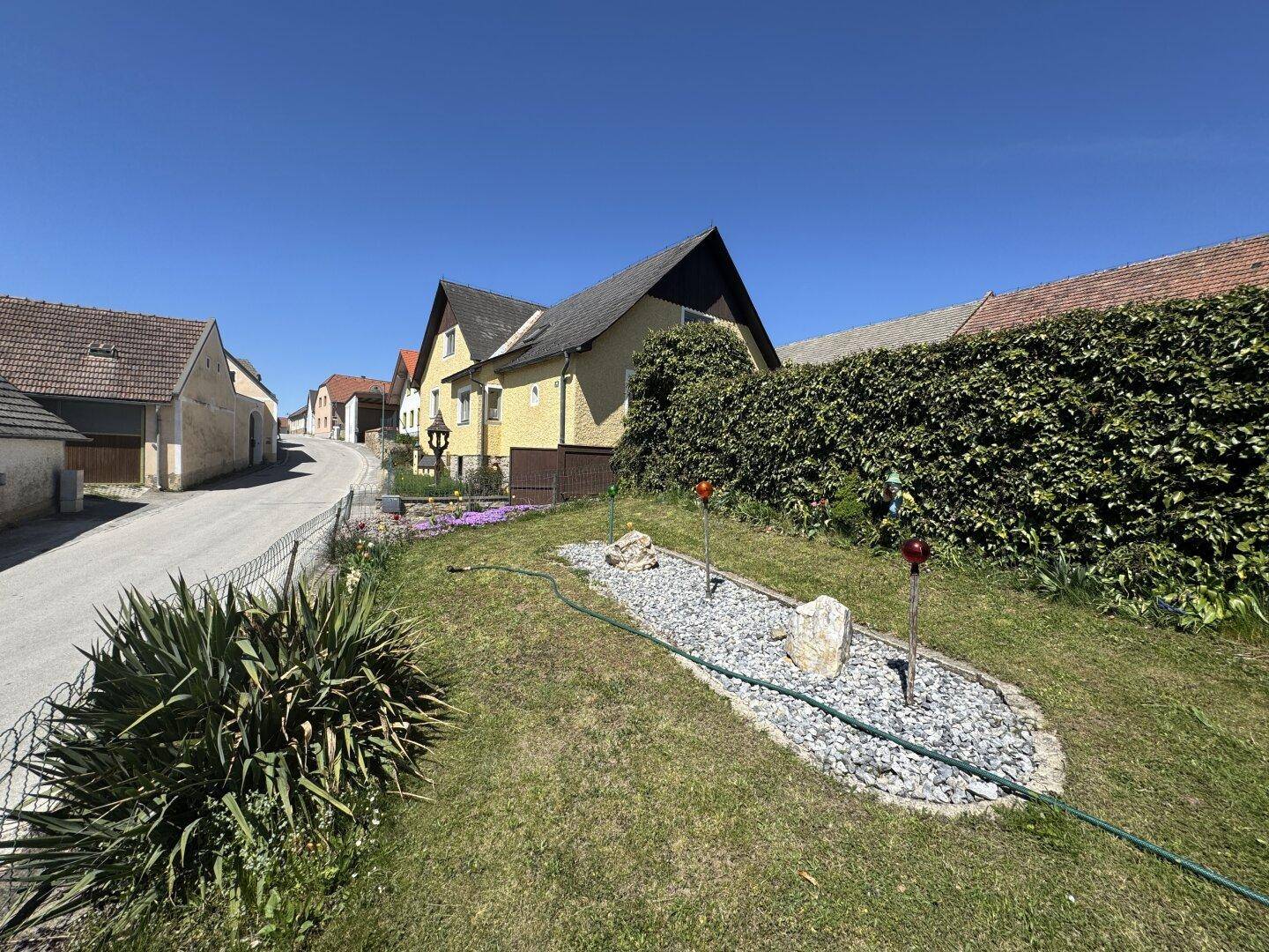 Gepflegter Vorgarten mit Zierkies und grüner Hecke vor dem gelben Wohnhaus.