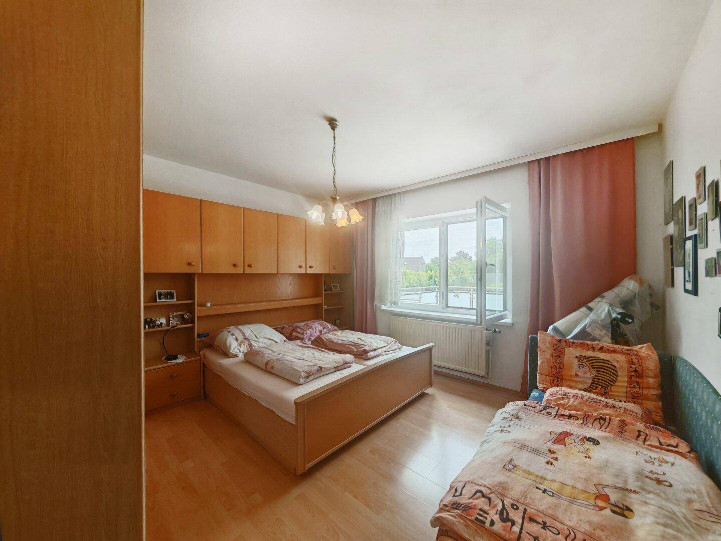 Schlafzimmer mit Doppelbett, integrierten Holzschränken und einem Fenster, das viel Tageslicht hereinlässt.