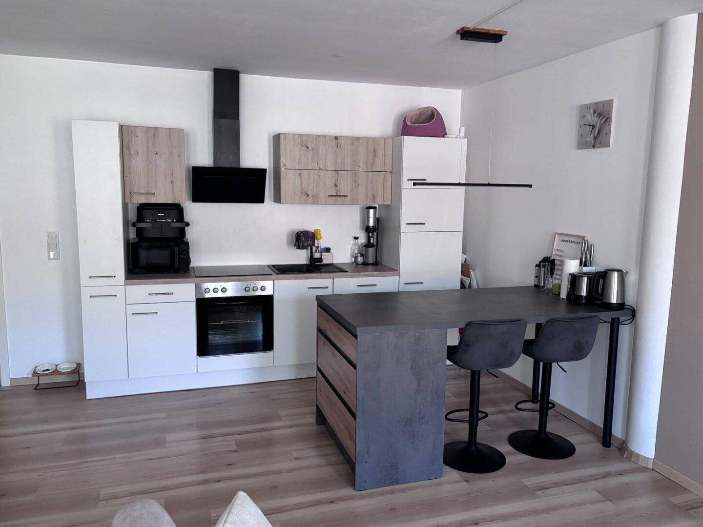 Moderne Küche mit weißen und holzfarbenen Schränken, Kochinsel und integrierten Geräten.
