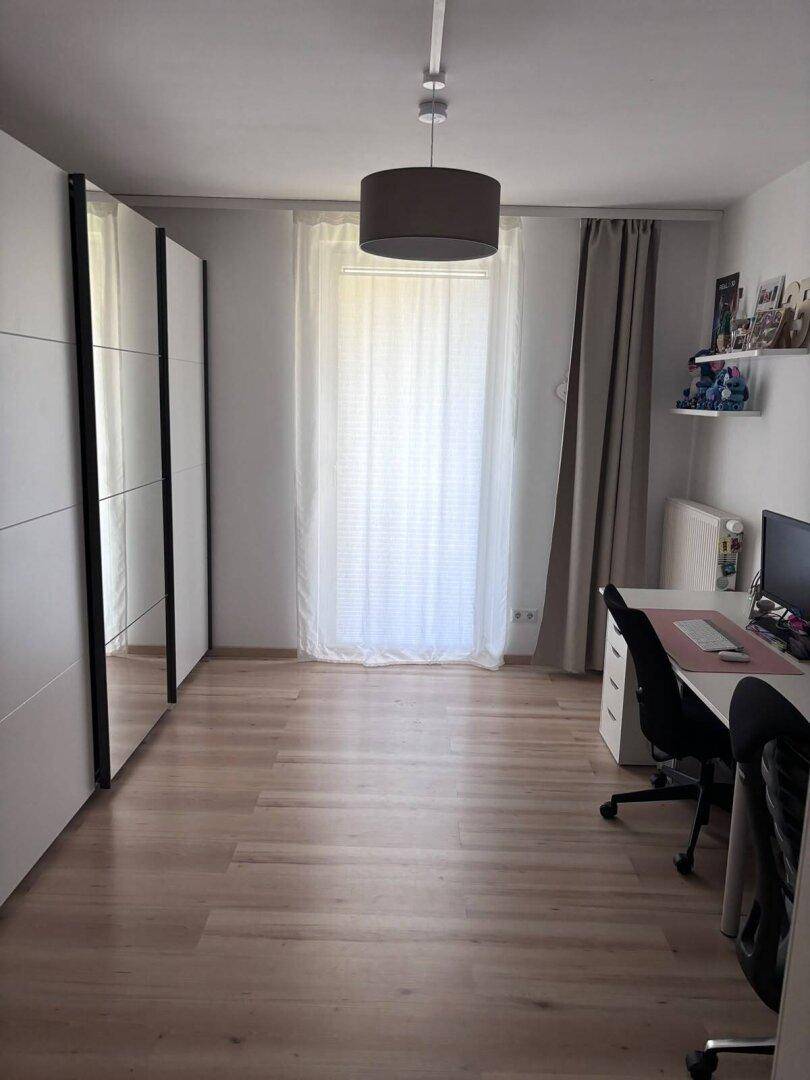 Helles Arbeitszimmer mit Laminatboden, weißen Schränken und einem großen Fenster.