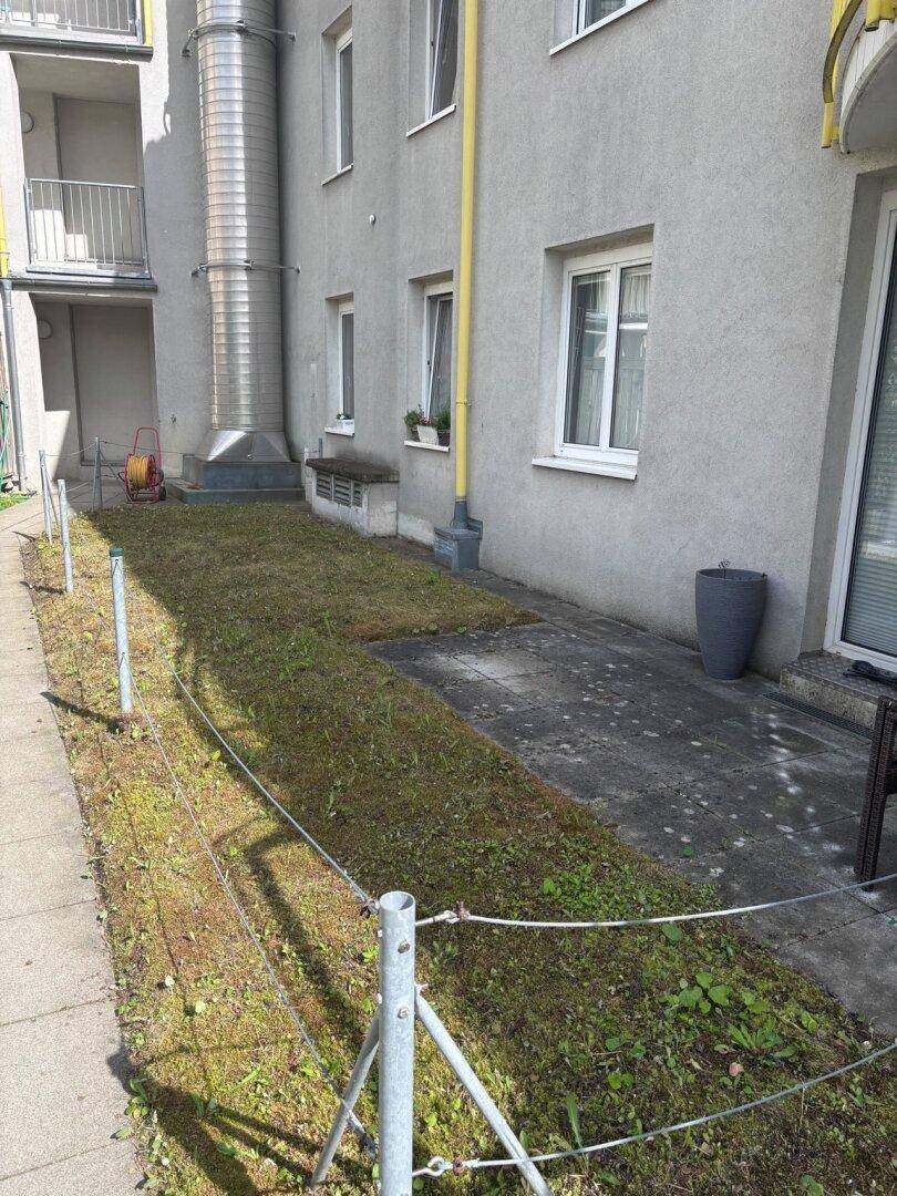 Kleiner Gartenbereich mit Rasenfläche und gepflasterter Terrasse neben dem Gebäude.