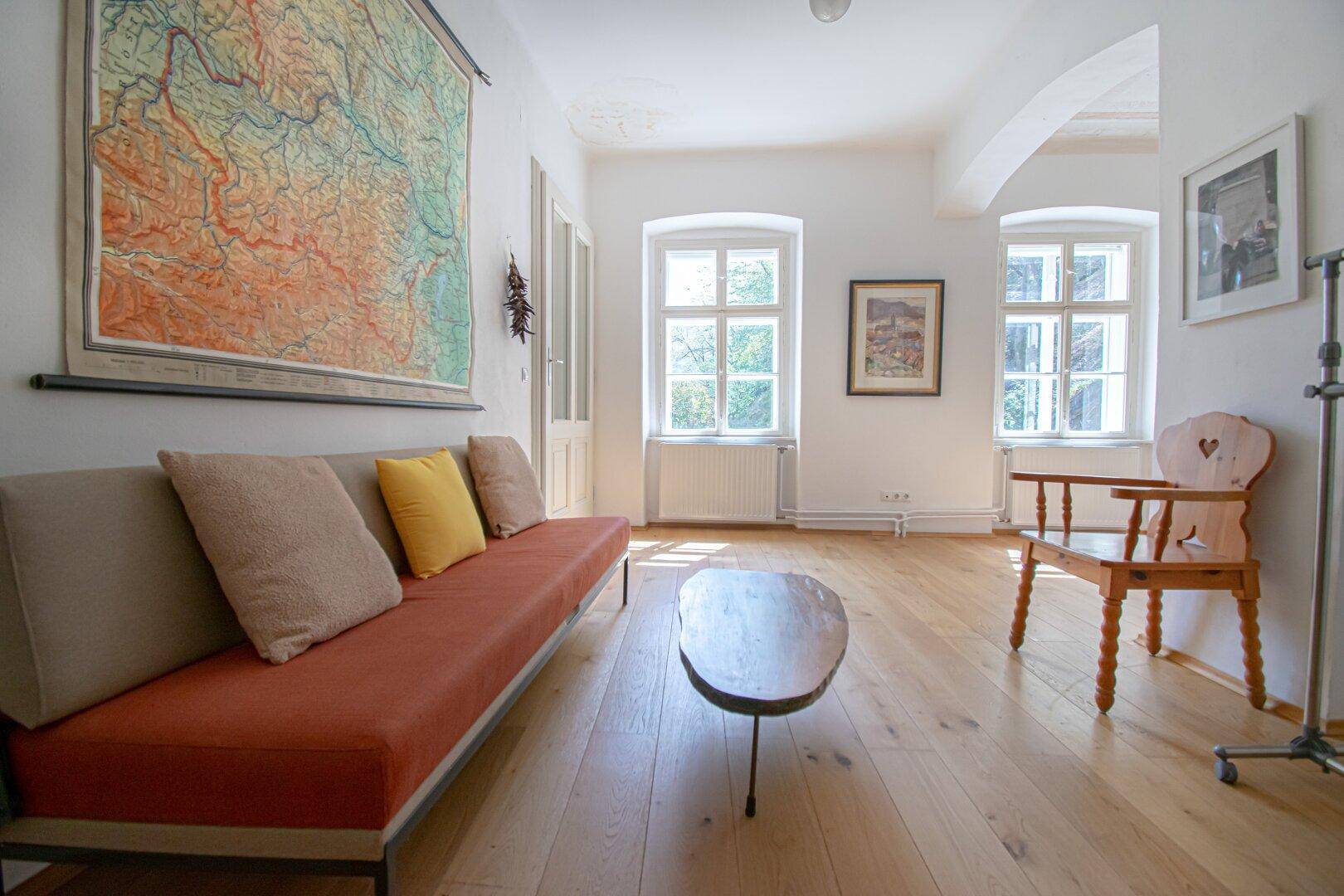 Helles Wohnzimmer mit Holzboden, beigem Sofa und großen Fenstern.