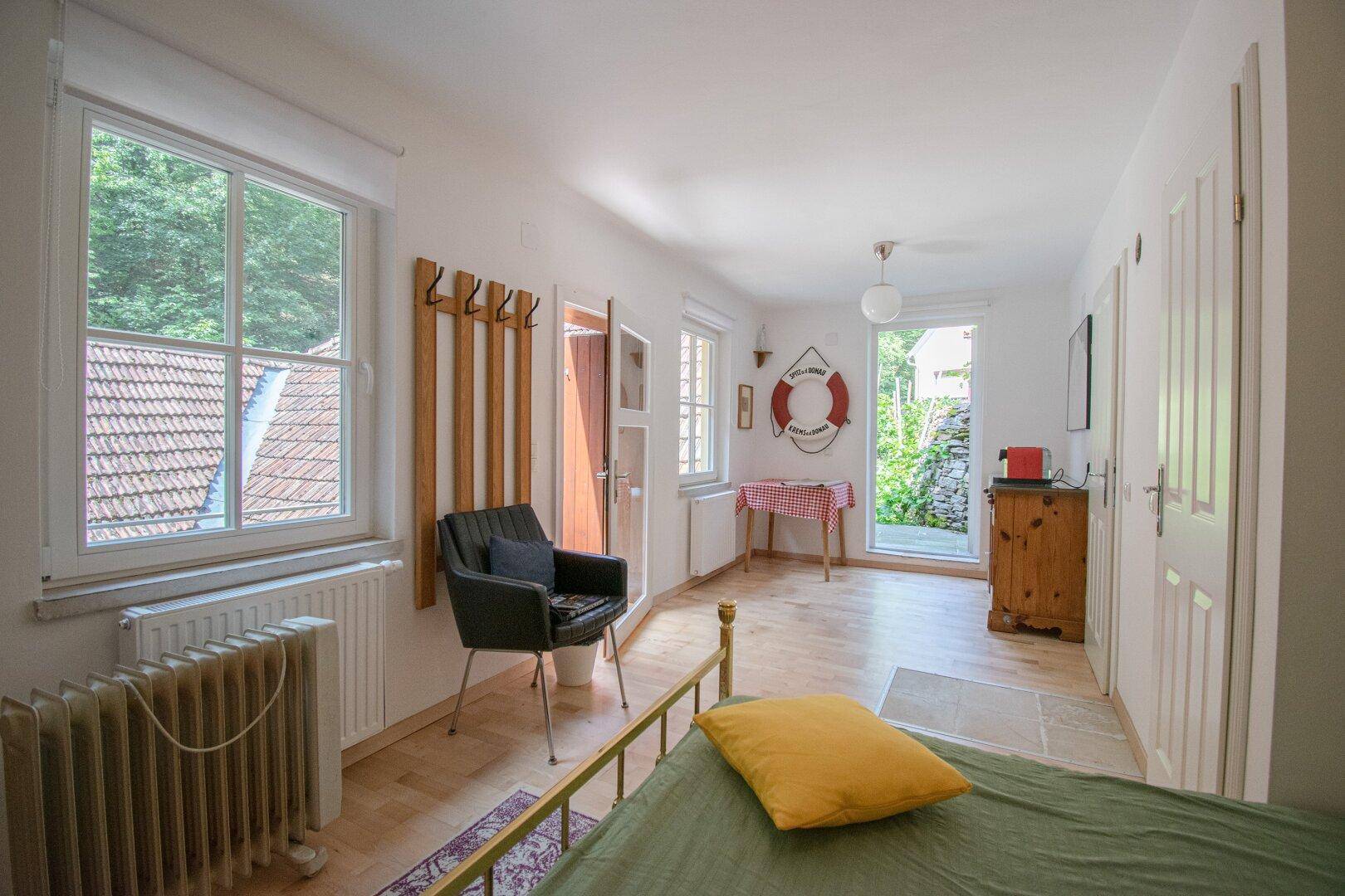 Schlichtes Schlafzimmer mit Holzboden, Fensterblick und Zugang zum Außenbereich.