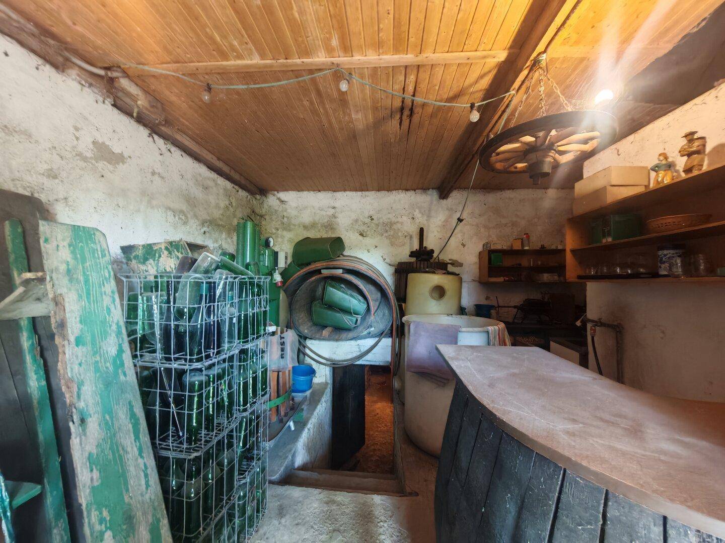 Rustikaler Lagerraum mit Holzdecke, Betonwänden und verschiedenen Flaschen sowie einem Fass.